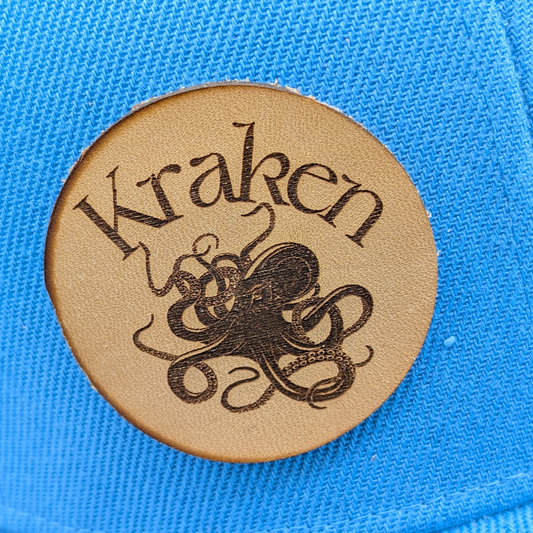 Up close view of Laser Engraved Leather Patch Text Kraken curved above the image of a Kraken. Kraken Viking Hat