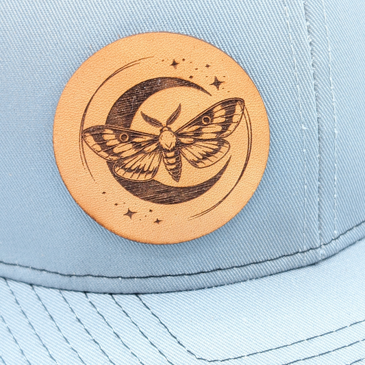 Up Close view of leather Laser Engraved Tan Patch on right side has a luna moth in front of a crescent moon. Mesh in back is a dark grey, stitching on bill is dark grey.