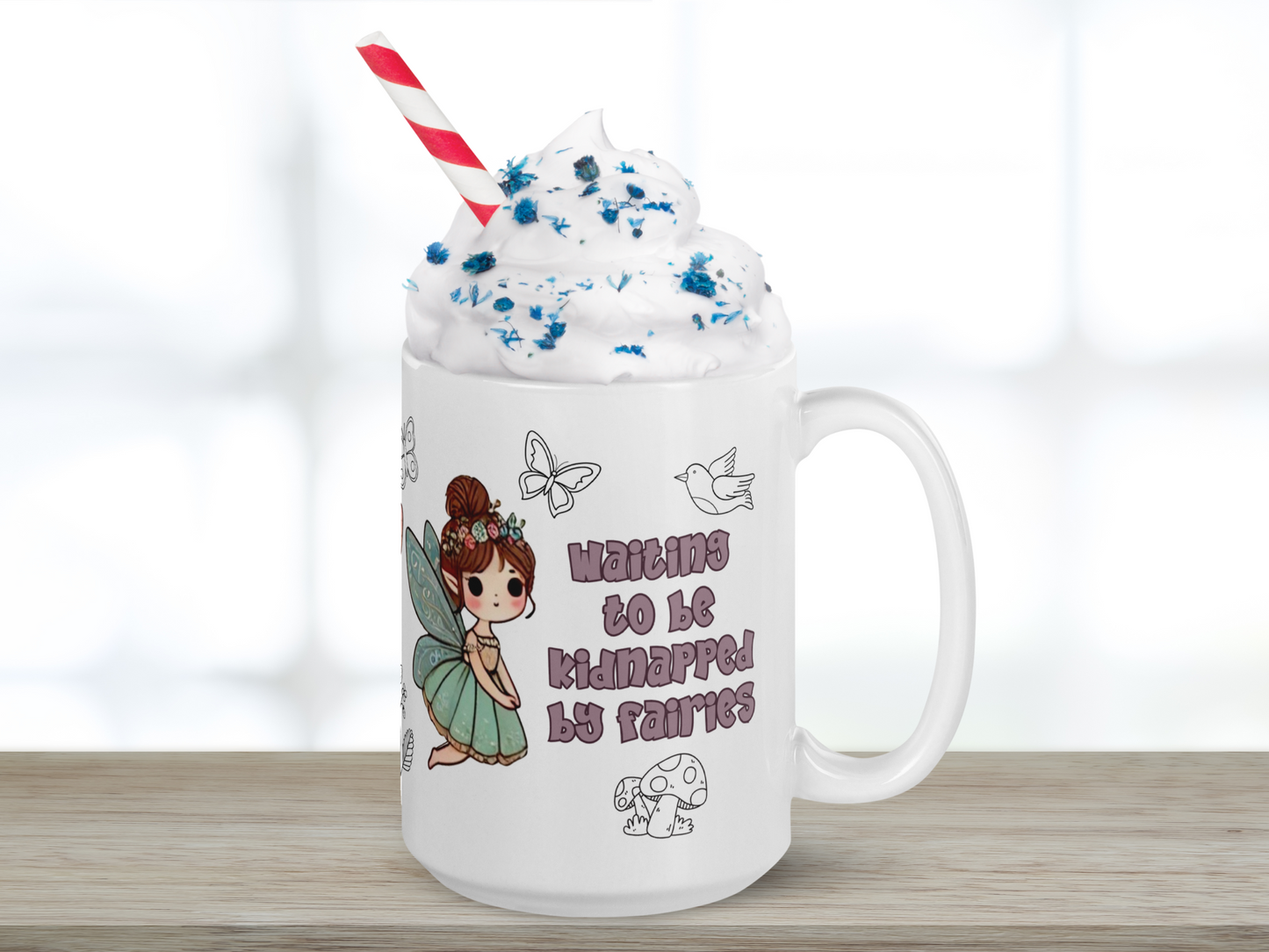 White Ceramic Mug handle to the right filled with peaks of whip cream, blue sprinkles, and a red and white paper straw. This Fairy mug shows text in a dusky purple "Waiting to be kidnapped by fairies". Above to the right is the outline of a bird and to the left is the outline of a flower. Below the text is the outline of mushrooms. To the left is a flying fairy with blue butterfly wings. A blue dress, brunette hair in a un with flowers and pointed ears. Fantasy Bookish Mug Gift for Her
