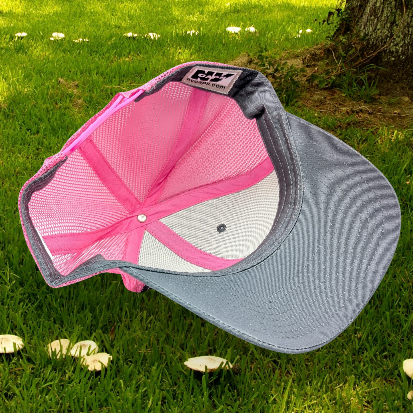 Bottom inside view of Grey and Pink Trucker hat with hot pink stitching on the bill. Front and bill of hat are grey and the back is hot pink mesh. Large round white patch is on the right side of the hat. Patch has the word Love in bubble letters. The o is a crescent moon with a fairy sitting inside it.