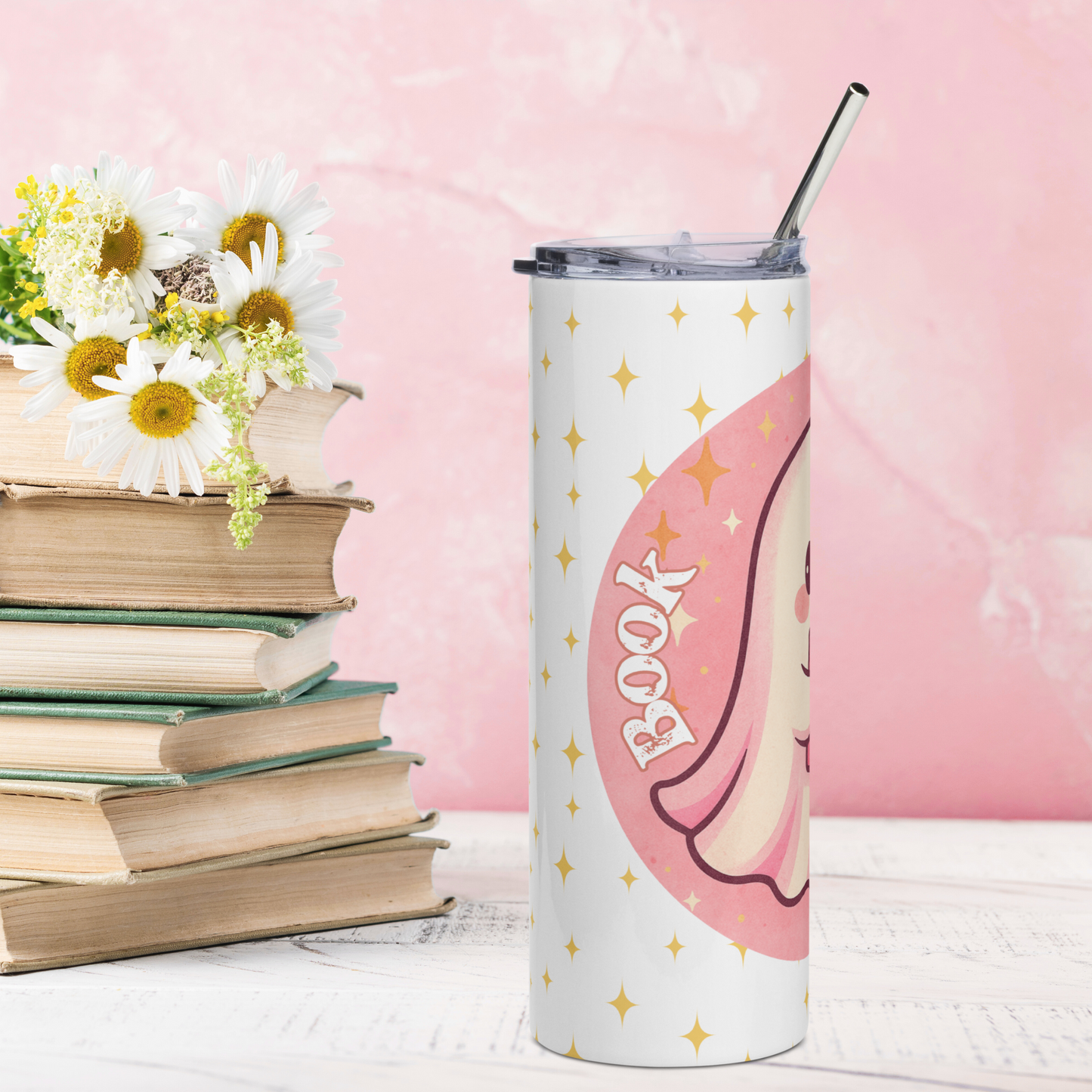 Left side view of Pink Coquette Book Ghost Stainless Steel Tumbler on White Background. Bubblegum pink circle with white ghost with pink shadows and rosy cheeks. The ghost is holding a pink book that is open and is reading. In white text to the Left Book. There are yellow stars in the background on the white. BPA free plastic lid is leaning on the right side of the water bottle. Whimsical Ghost Reading Book