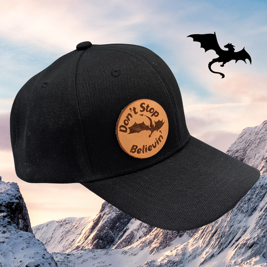 Left side view of Black Baseball Style Hat with Laser Engraved tan leather patch. Leather Patch is on the left side of the hat when looking at it. On the patch is a s flying dragon with the text Don't Stop Believin'Fantasy dragon Hat