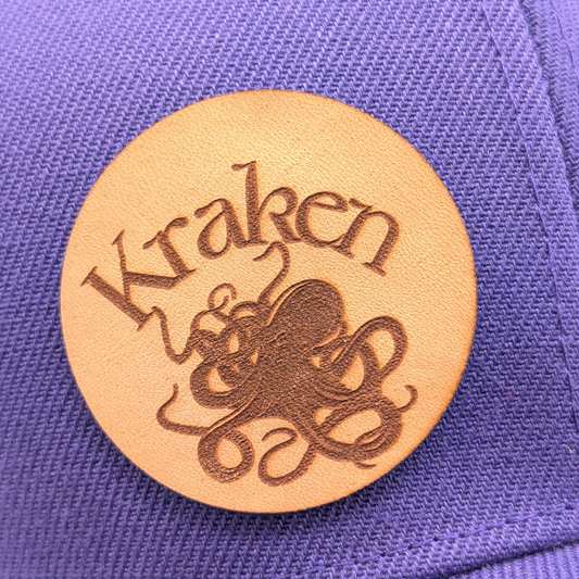 Up close view of Laser Engraved Leather Patch Text Kraken curved above the image of a Kraken. Kraken Viking Hat