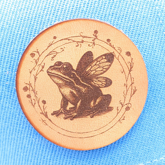 Up close view of laser engraved patch of a Fairy frog in a circle of vines. Fantasy Core Vintage Fairy Tale Princess and the Frog
