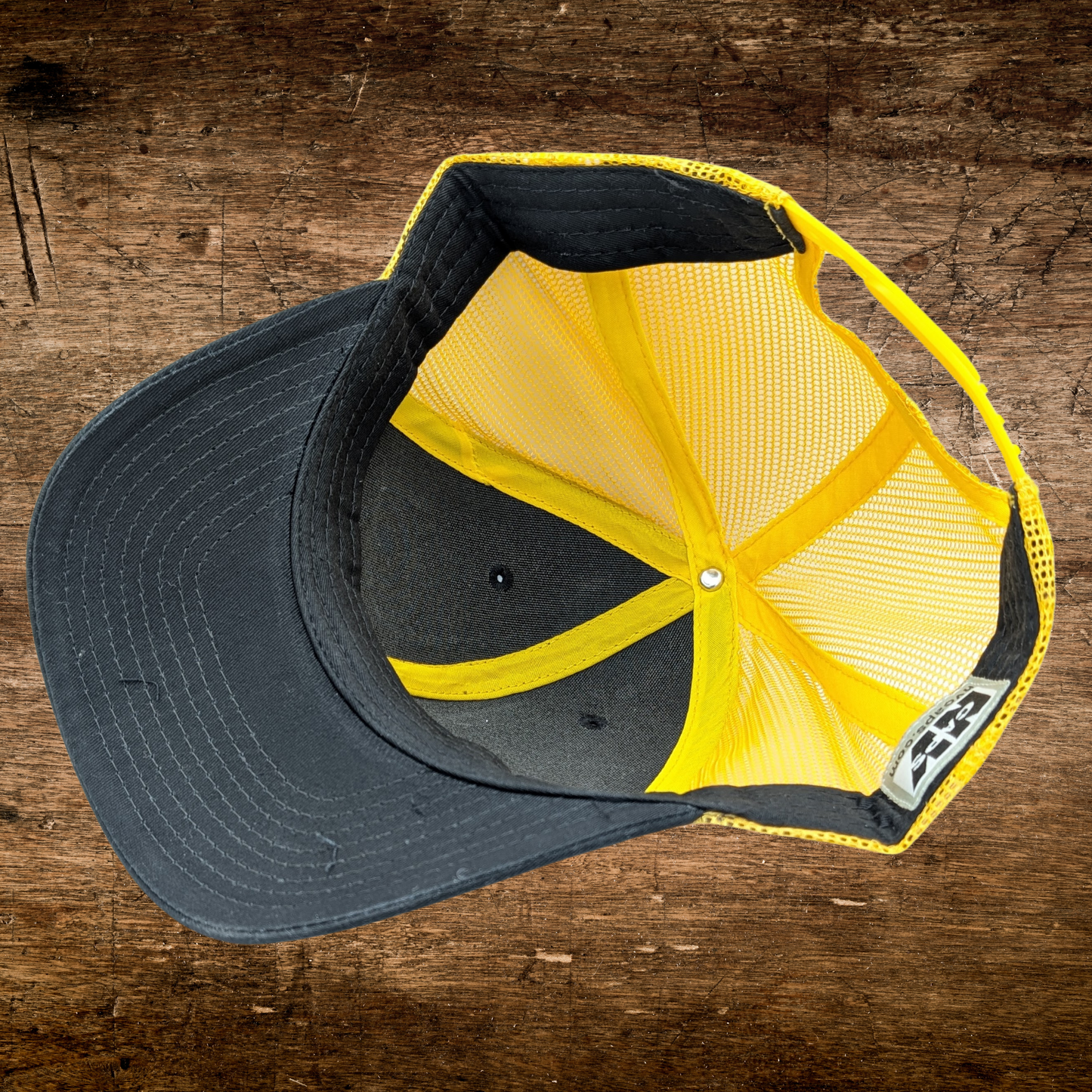 Bottom inside view of Poisoned Apple Enthusiast Dark Snow White Fairy Tale Hat. Hat is a gold/yellow mesh the bill and front is grey with gold/yellow stitching. Bottom of bill has grey stitching. You can see the cotton sweatband on the interior of the hat.