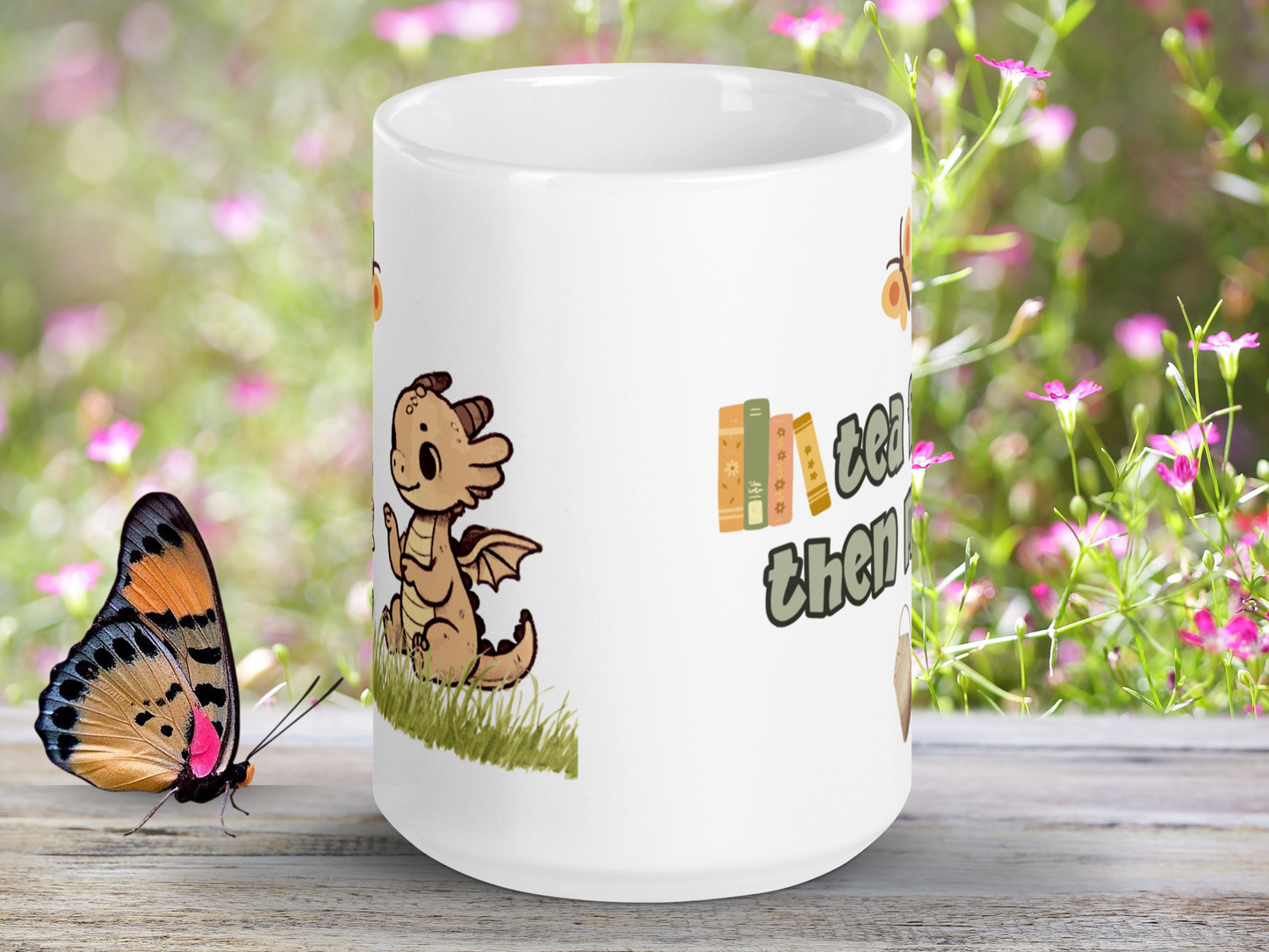 What dragon mug with handle to the back. You can see the side view of the pink dragon sitting in the grass and to the right see books above the word then.