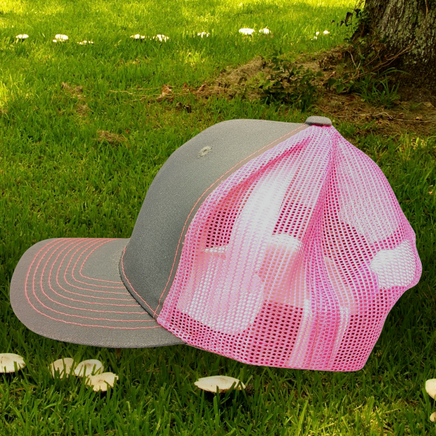 Left side view of Grey and Pink Trucker hat with hot pink stitching on the bill. Front and bill of hat are grey and the back is hot pink mesh.