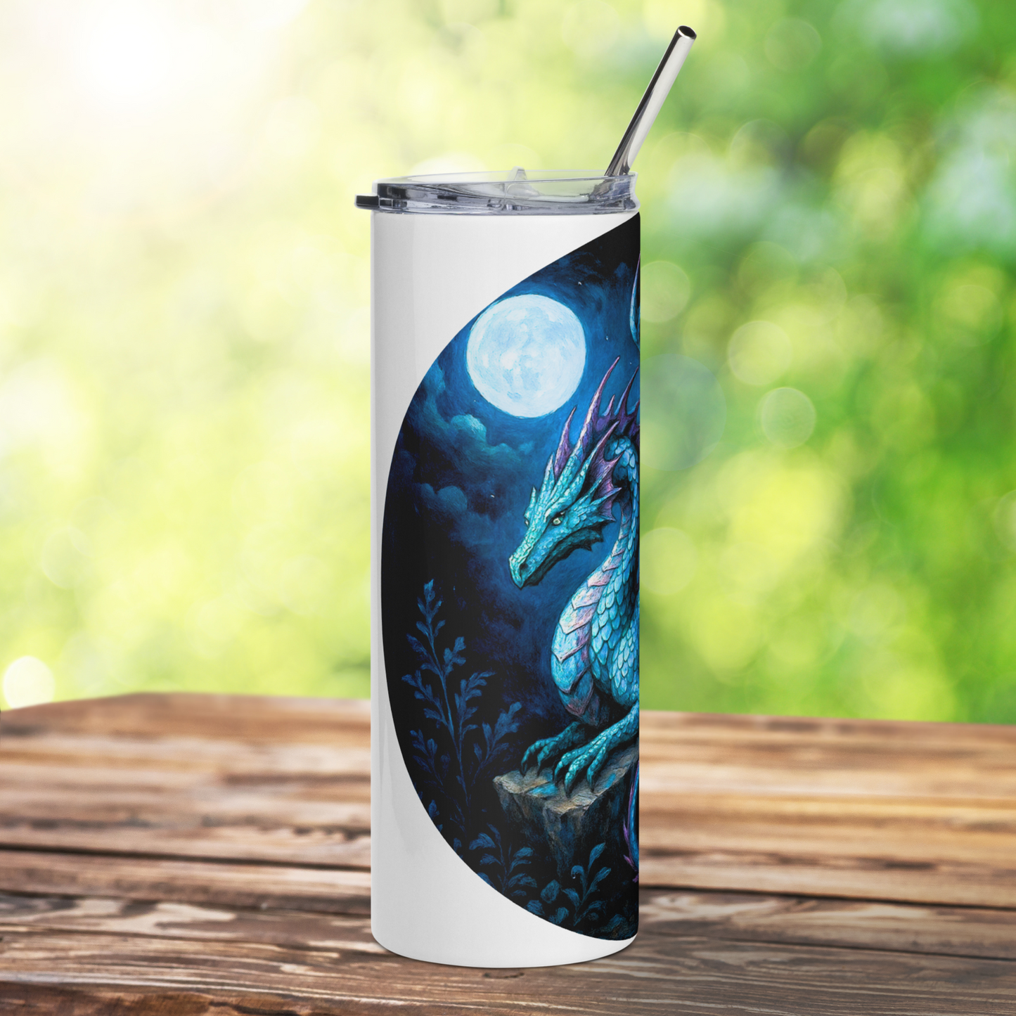 Insulated stainless steel fantasy dragon tumbler. This is a left side view of a blue dragon with purple highlights on the wings, horns, and tail. The dragon is resting on an outcrop of rocks at night. There is a dark cloudy sky with a full moon. Graphic is in blues and purple. You can see the stainless steel straw sticking up from the tumbler. The graphic is on a white tumbler.