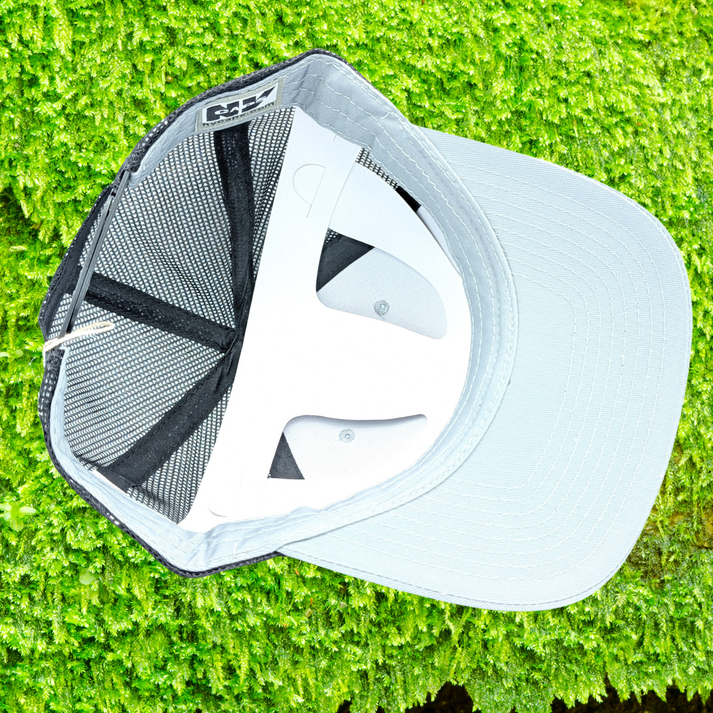 Bottom inside view of Grey Snapback Trucker Hat Leather Laser Engraved Tan Patch on right side has a luna moth in front of a crescent moon. Mesh in back is a dark grey, stitching on bill is dark grey.