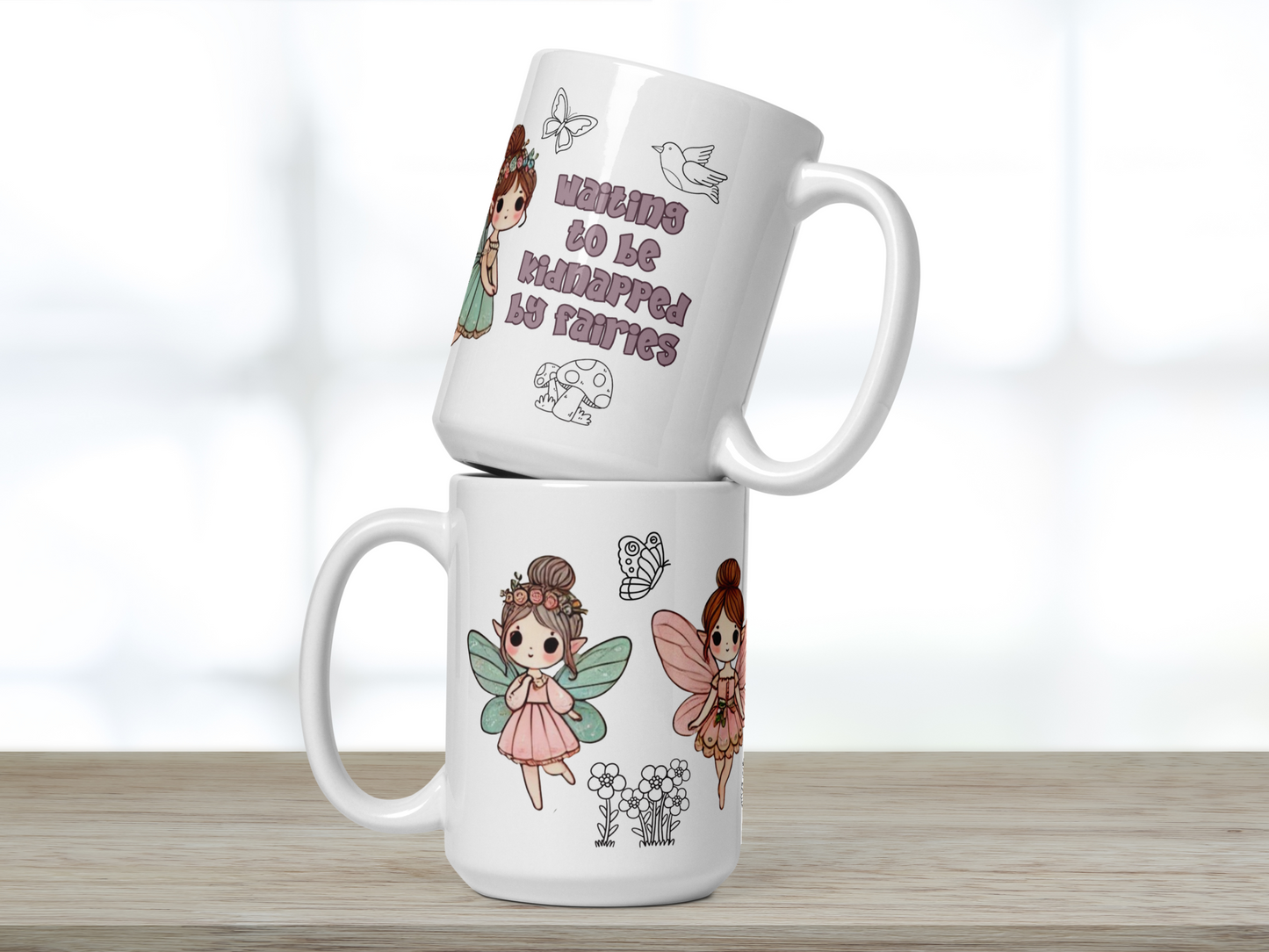 White 15 oz ceramic mug. Image shows two mugs stacked on top of each other handles to either direction. Top mug handle to right in dusky purple text says waiting to be kidnapped by fairies. Above is a butterfly and bird and below is a mushroom. You can see the side of a fairy. Bottom mug handle to the left. You see a walking fairy in a pink dress, blue wings, hair in a bun with flowers. You see the side of another fairy to the right with pink wings and dress. Between the fairies are flowers and a butterfly