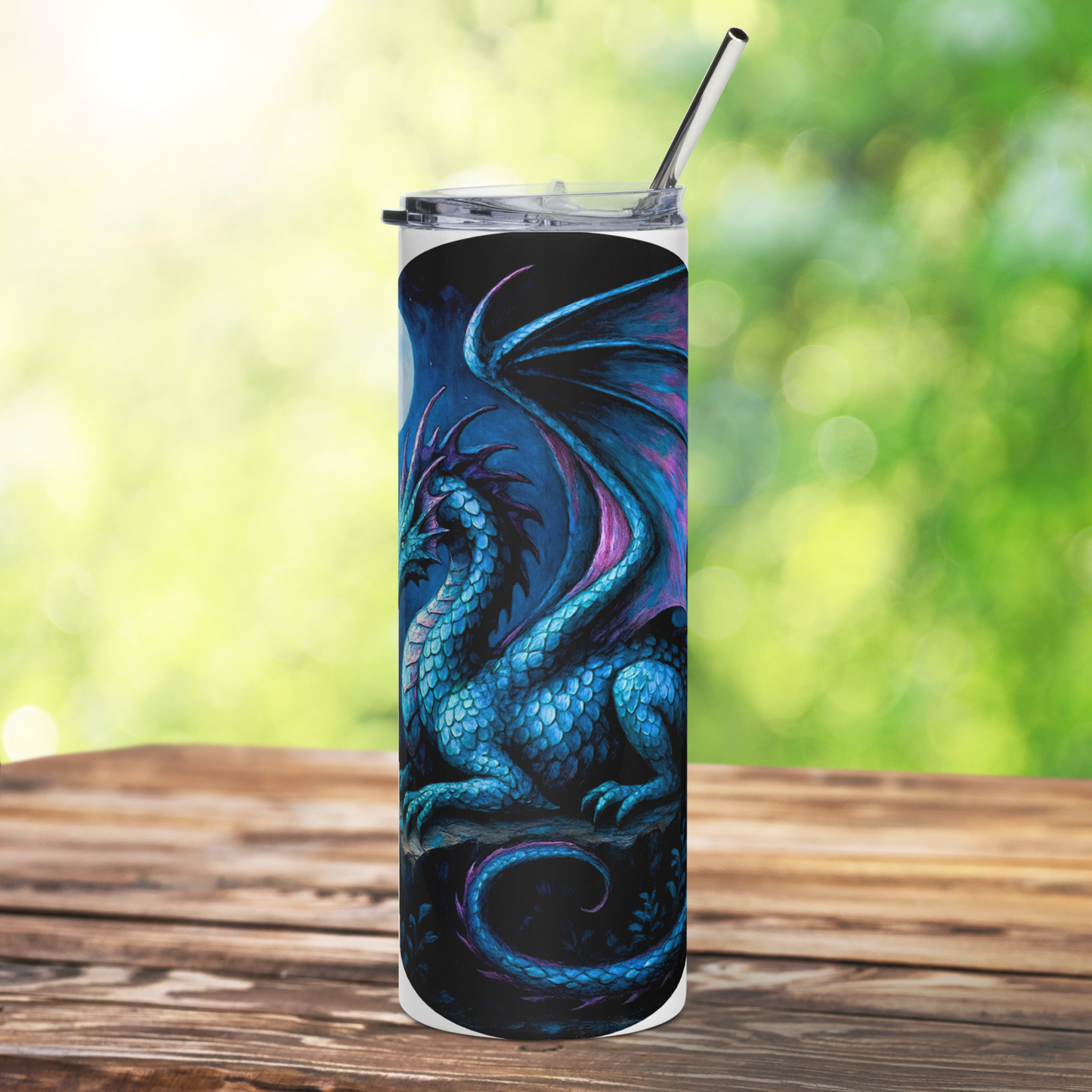 Insulated stainless steel fantasy dragon tumbler. This is a front view of a blue dragon with purple highlights on the wings, horns, and tail. The dragon is resting on an outcrop of rocks at night. There is a dark cloudy sky with a full moon. Graphic is in blues and purple. You can see the stainless steel straw sticking up from the tumbler. The graphic is on a white tumbler.