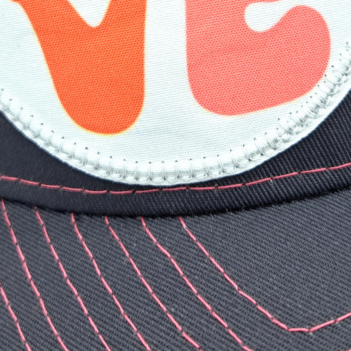 Up close view of the bottom of the patch and part of the bill. Grey and Pink Trucker hat with hot pink stitching on the bill. Front and bill of hat are grey and the back is hot pink mesh. Large round white patch is on the right side of the hat. Patch has the word Love in bubble letters. The o is a crescent moon with a fairy sitting inside it.