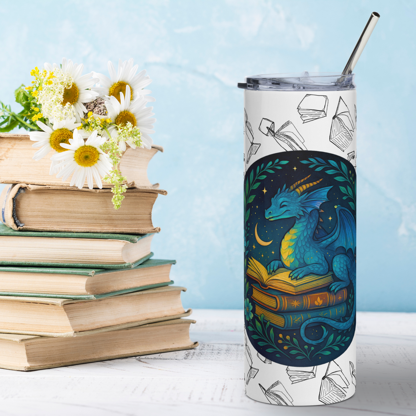Front view Book Dragon Graphic on White stainless steel 20 oz tumbler. Blue book dragon with horns perched on top of a stack of books. The top book is open for reading. Behind the dragon is the night sky with a crescent moon. Bordering the dragon are vines and flowers. Behind the circle graphic are black outlines of books surrounding the entire tumbler. You see the metal straw sticking out of the top. Bookish Gift for Fantasy Lovers
