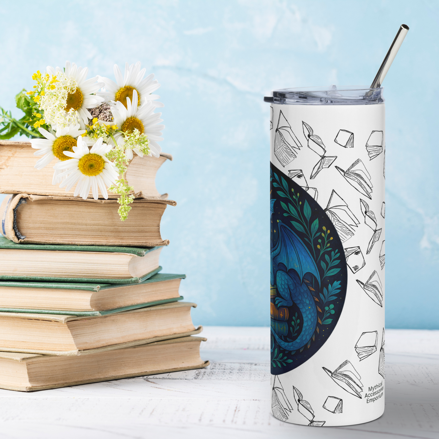 Right side view Book Dragon Graphic on White stainless steel 20 oz tumbler. Blue book dragon with horns perched on top of a stack of books. The top book is open for reading. Behind the dragon is the night sky with a crescent moon. Bordering the dragon are vines and flowers. Behind the circle graphic are black outlines of books surrounding the entire tumbler. You see the metal straw sticking out of the top. Librarian Teacher Gift