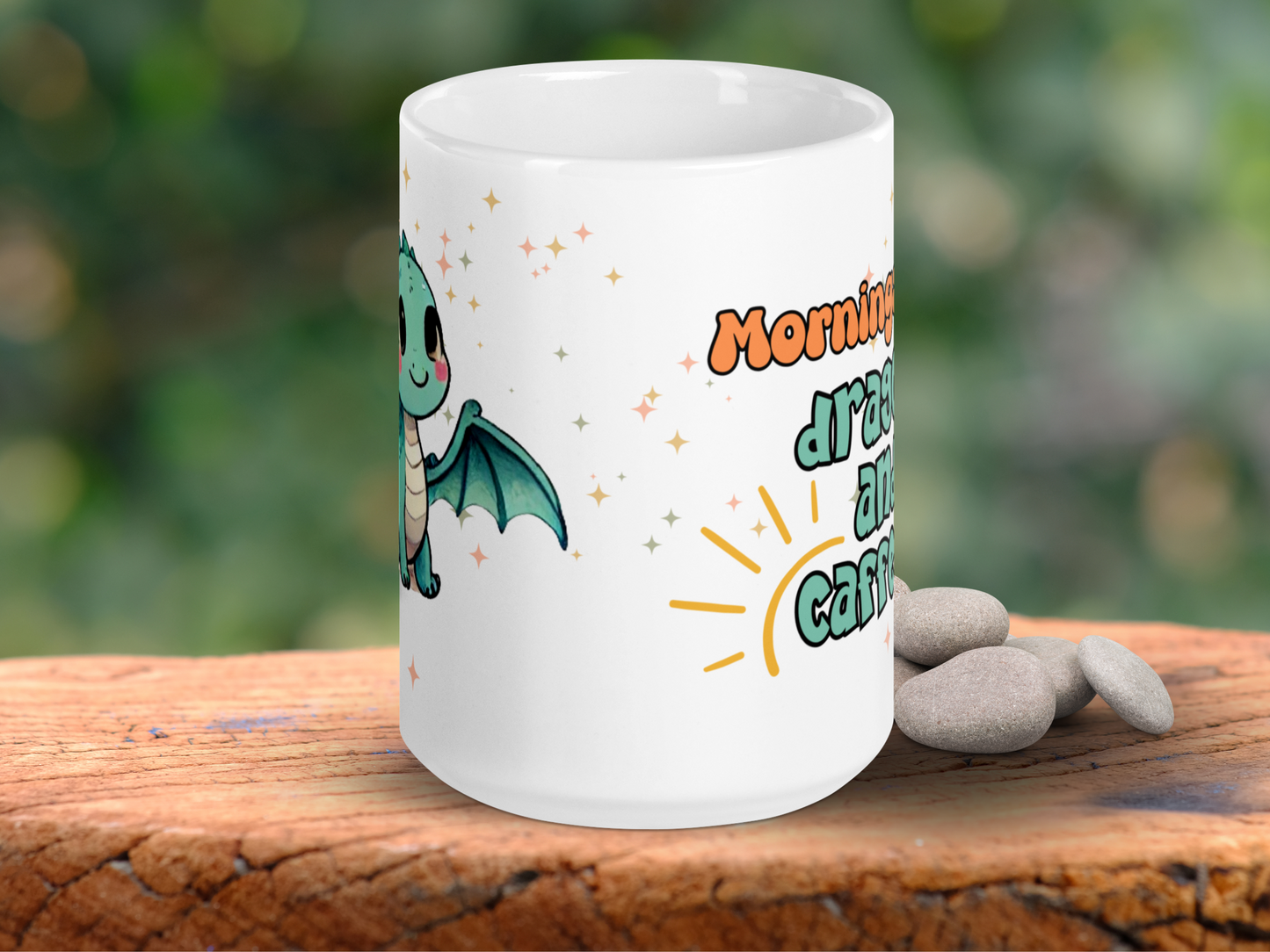 Dragon mug handle to the back. You can see the wing of the green kawaii baby dragon. You can see to the right part of the text, "Mornings, drag, a, and caff. part of the text Mornings need dragons and caffeine. The outline of a sun wraps around the beginning of the word caffeine. You can see magic stars in gold, silver, and rose gold.