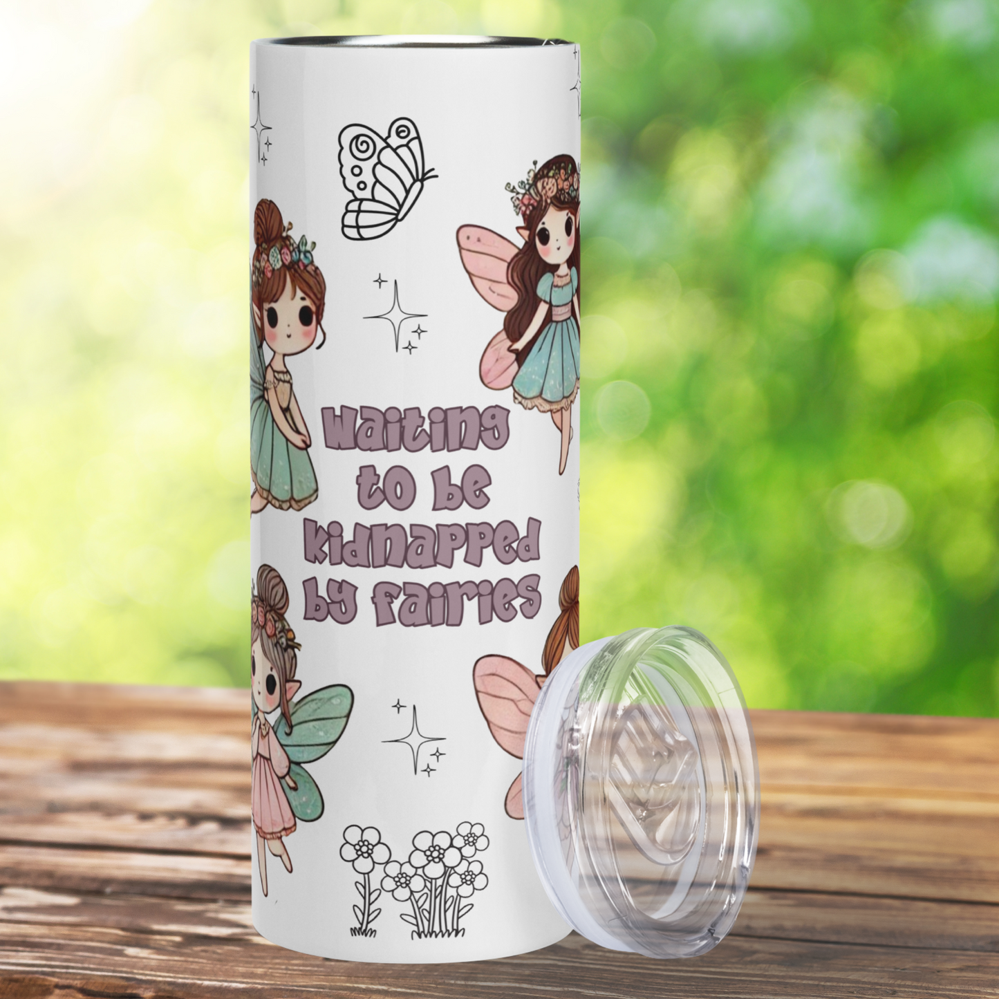 Kidnapped by Fairies 20 oz Stainless Steel Tumbler front view with lid leaning on the right side. Front view shows the text, "Waiting to be Kidnapped by Fairies" in lilac. At the top is the doodle of a butterfly. At the bottom is a doodle of a group of daisies. On the left you see the sides of two fairies and on the right you see the left sides of two fairies. Whimsigoth Bookish Merch