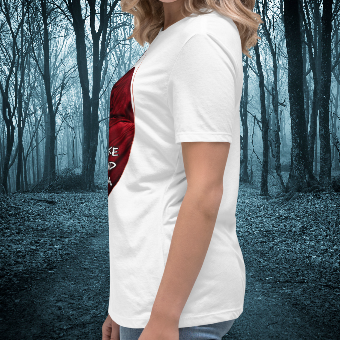 Red Riding Hood Women's Dark Fantasy T-Shirt. Left side View White Graphic Tee on Model. Oval frame with thin red border. From the left side you can see part of the red cloak and hood. Short sleeves and hem are visible along with the side seam of the shirt. Bookish Merch