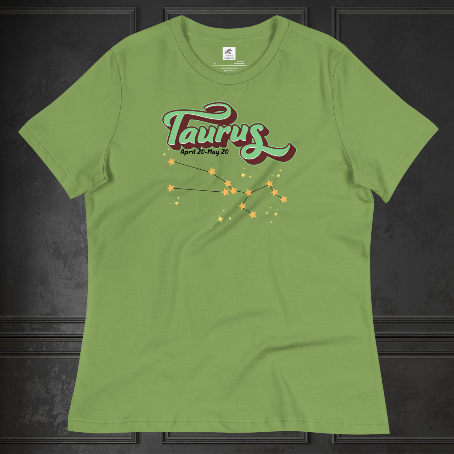 Front view of Leaf green Taurus Tee laying flat on a black surface. You can see the crew neck collar and short sleeves of the t shirt. This Astrology T-Shirt has the word Taurus in large leaf green script shadowed in deep brown for a 3-D effect. Below this it Says April 20-May 20. At the bottom is the star constellation for Taurus with yellow stars connected by a black line and smaller stars surrounding the constellation. The perfect April or May Birthday Gift for Her or yourself.