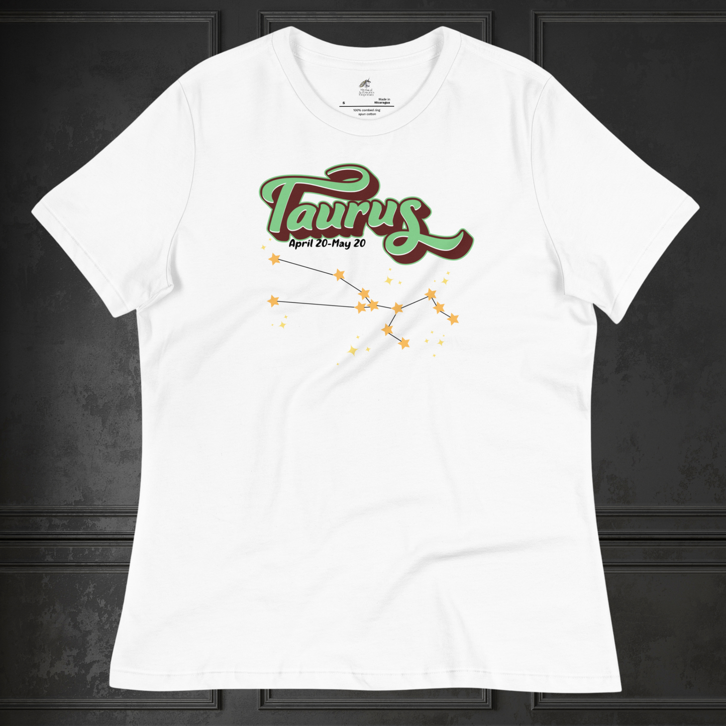 Front view of white Taurus Tee laying flat on a black surface. You can see the crew neck collar and short sleeves of the t shirt. This Astrology T-Shirt has the word Taurus in large leaf green script shadowed in deep brown for a 3-D effect. Below this it Says April 20-May 20. At the bottom is the star constellation for Taurus with yellow stars connected by a black line and smaller stars surrounding the constellation. The perfect April or May Birthday Gift for Her or yourself.