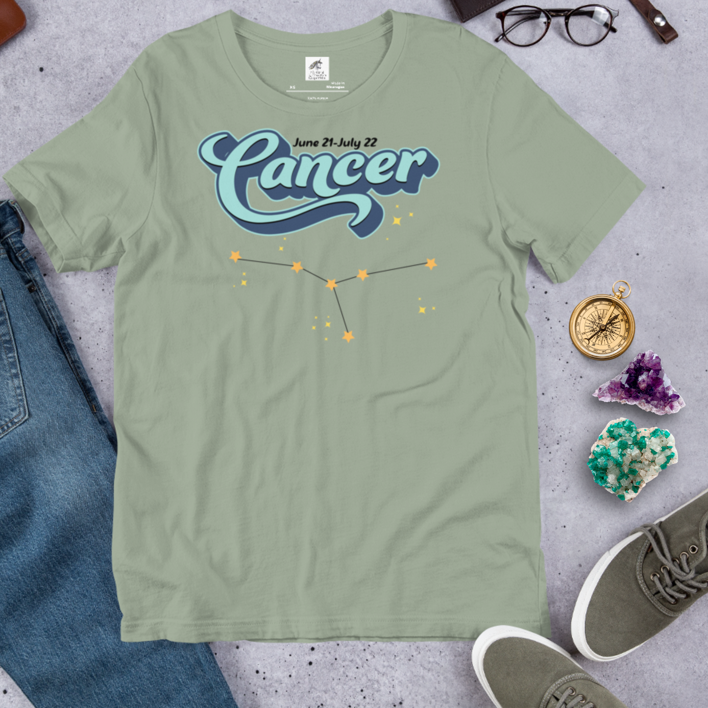 Front view of flat sage men's Cancer Tee. This astrology Cancer T-Shirt has the word Cancer in large light blue script shadowed in deep blue for a 3-D effect. Above this it Says June 21-July 22. Under Cancer is the zodiac star constellation with yellow stars connected by a black line and lighter yellow smaller stars surrounding this. The perfect June or July Birthday Gift for him or yourself.