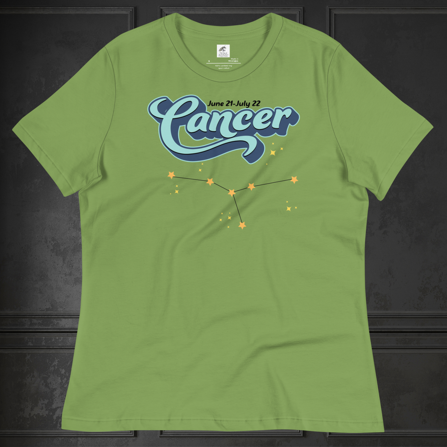 Front view of flat lay leaf green women's Cancer Tee. This astrology Cancer T-Shirt has the word Cancer in large light blue script shadowed in deep blue for a 3-D effect. Above this it Says June 21-July 22. Under Cancer is the zodiac star constellation with yellow stars connected by a black line and lighter yellow smaller stars surrounding this. The perfect June or July Birthday Gift for Her or yourself.