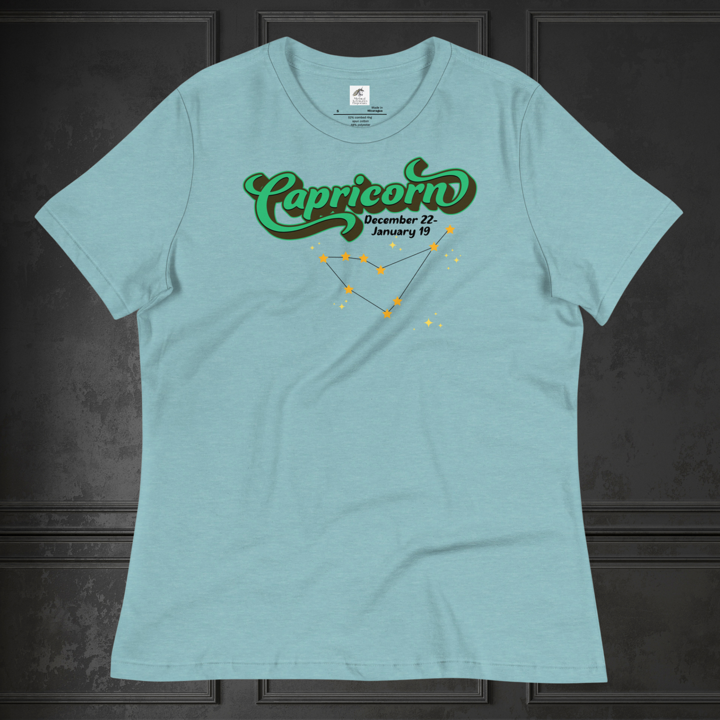 Front view of flat heather blue lagoon women's Capricorn Tee. This astrology T-Shirt has the word Capricorn in a large green script shadowed in black for a 3-D effect. Below this it Says December 22-January 19. Under Capricorn is the zodiac star constellation with yellow stars connected by a black line and lighter yellow smaller stars surrounding this. The perfect December or January Birthday Gift for Her or yourself.
