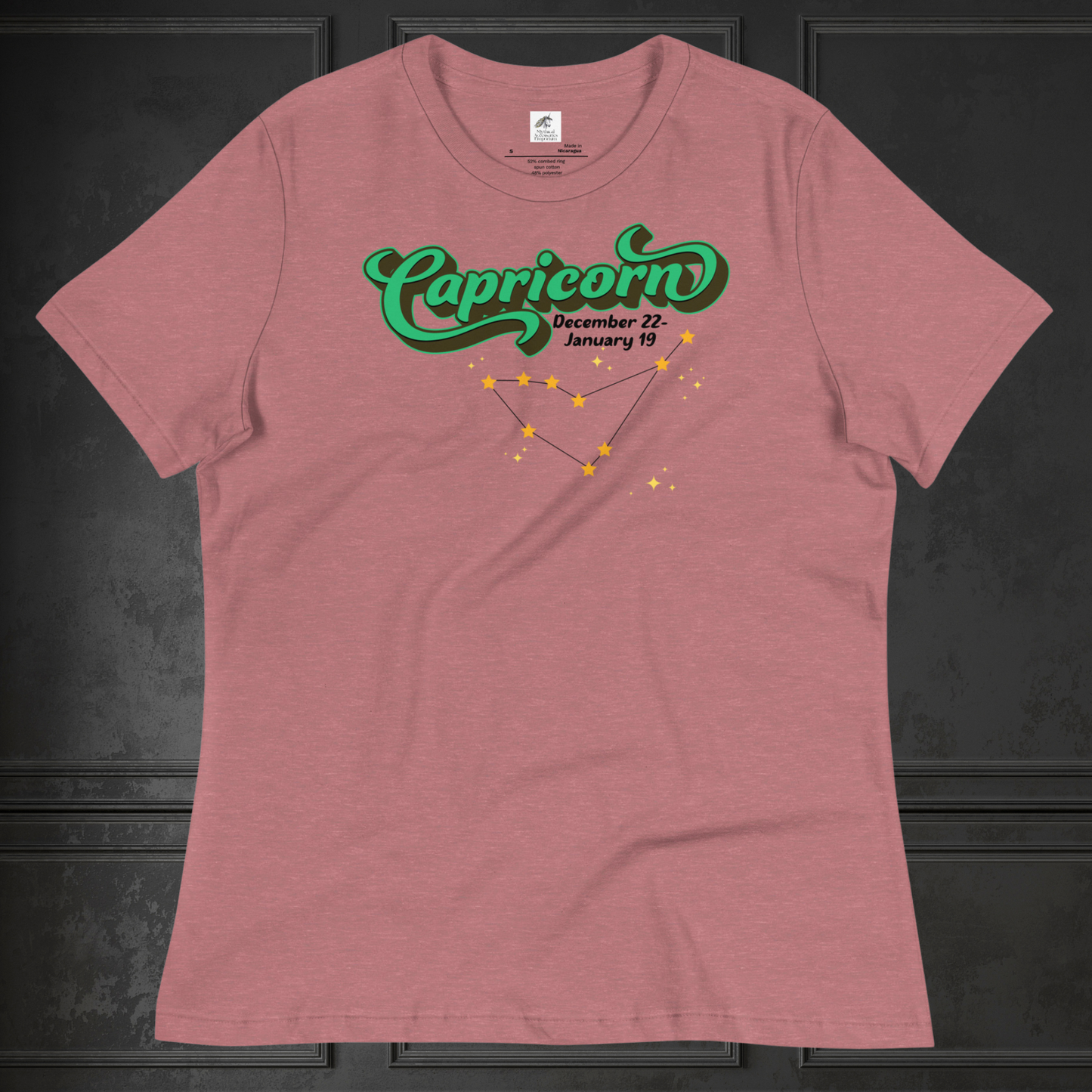 Front view of flat heather mauve women's Capricorn Tee. This astrology T-Shirt has the word Capricorn in a large green script shadowed in black for a 3-D effect. Below this it Says December 22-January 19. Under Capricorn is the zodiac star constellation with yellow stars connected by a black line and lighter yellow smaller stars surrounding this. The perfect December or January Birthday Gift for Her or yourself.