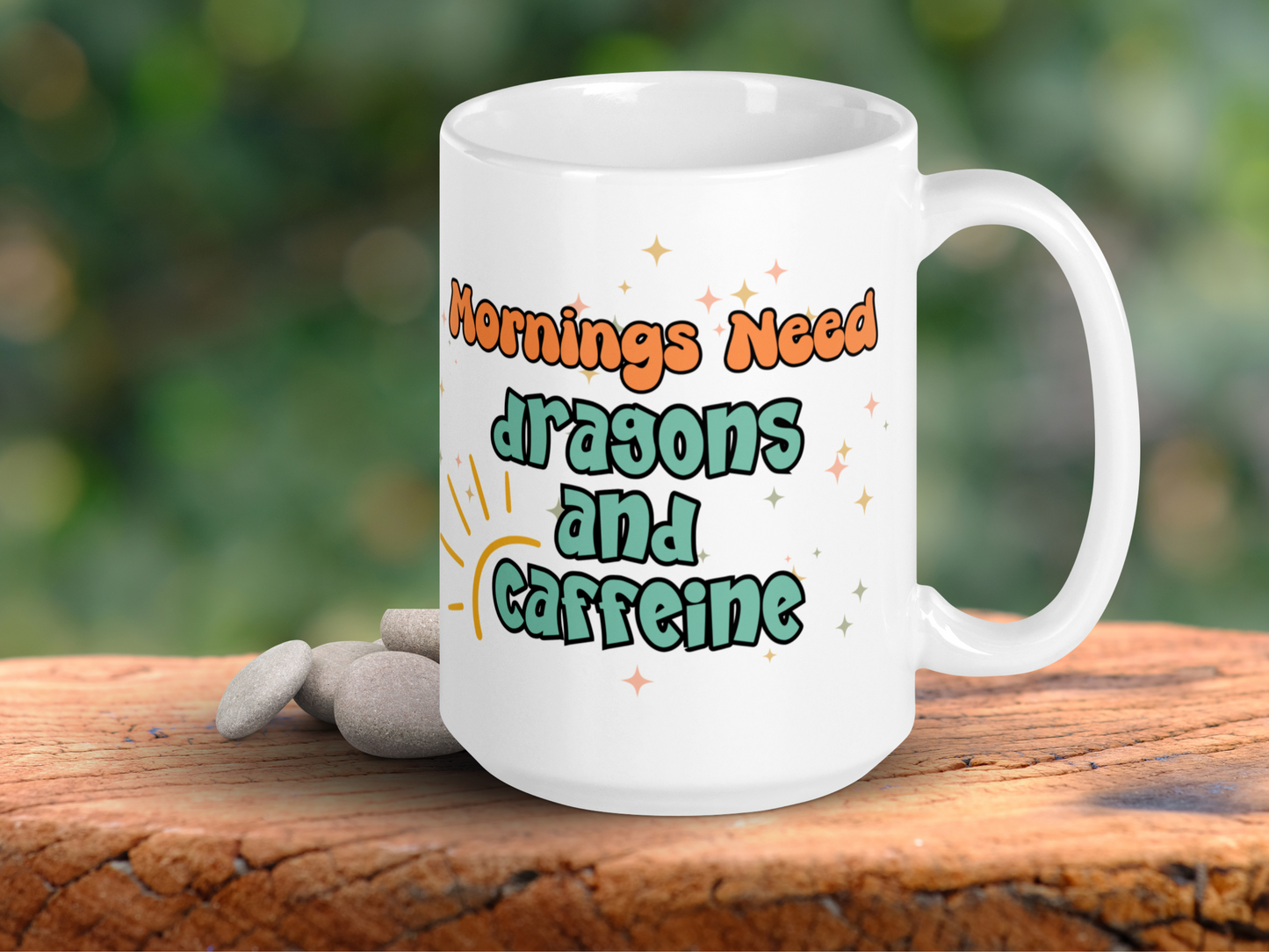 Dragon Coffee mug with handle to the right. You can see in tangerine orange, "Mornings Need". In pistachio green with a black outline the text "dragons and caffeine". Around the word caffeine and extending up is the outline of a sun. You can see gold, silver, and copper colored stars of magic.