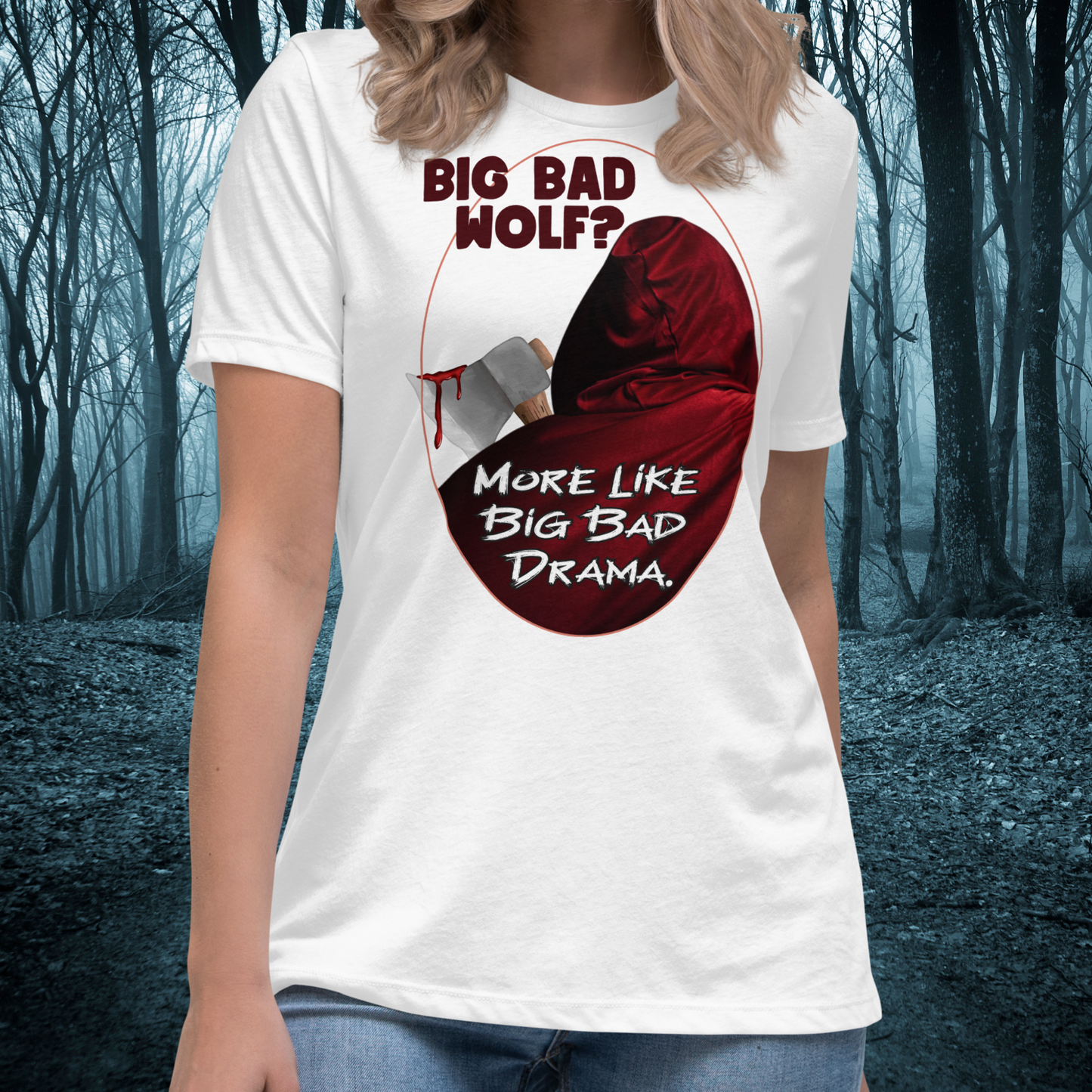 Red Riding Hood Women's Dark Fantasy T-Shirt. Front View White Graphic Tee on Model. Oval frame with thin red border. You can see the back of red riding hood with hood up. Bloody axe over her shoulder. Text Big Bad Wolf? More Like Big Bad Drama. Women's Feminist Bookish Shirt