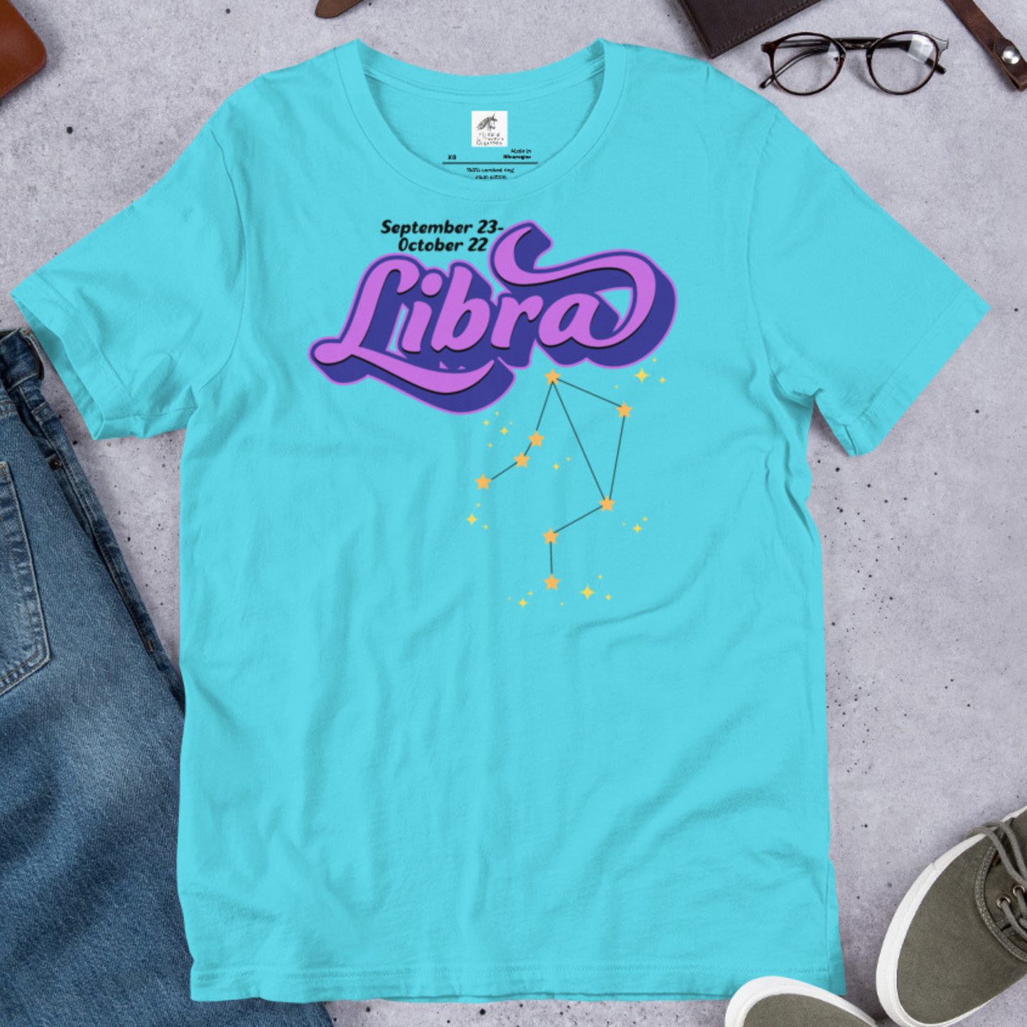 Flat front view of turquoise men's Libra Tee. This astrology Libra T-Shirt has the word Libra in large purple script shadowed in deep blue for a 3-D effect. Below this it Says September 23-October 22. Under Libra is the zodiac star constellation with yellow stars connected by a black line and lighter yellow smaller stars surrounding this. The perfect October or September Birthday Gift for him or yourself.