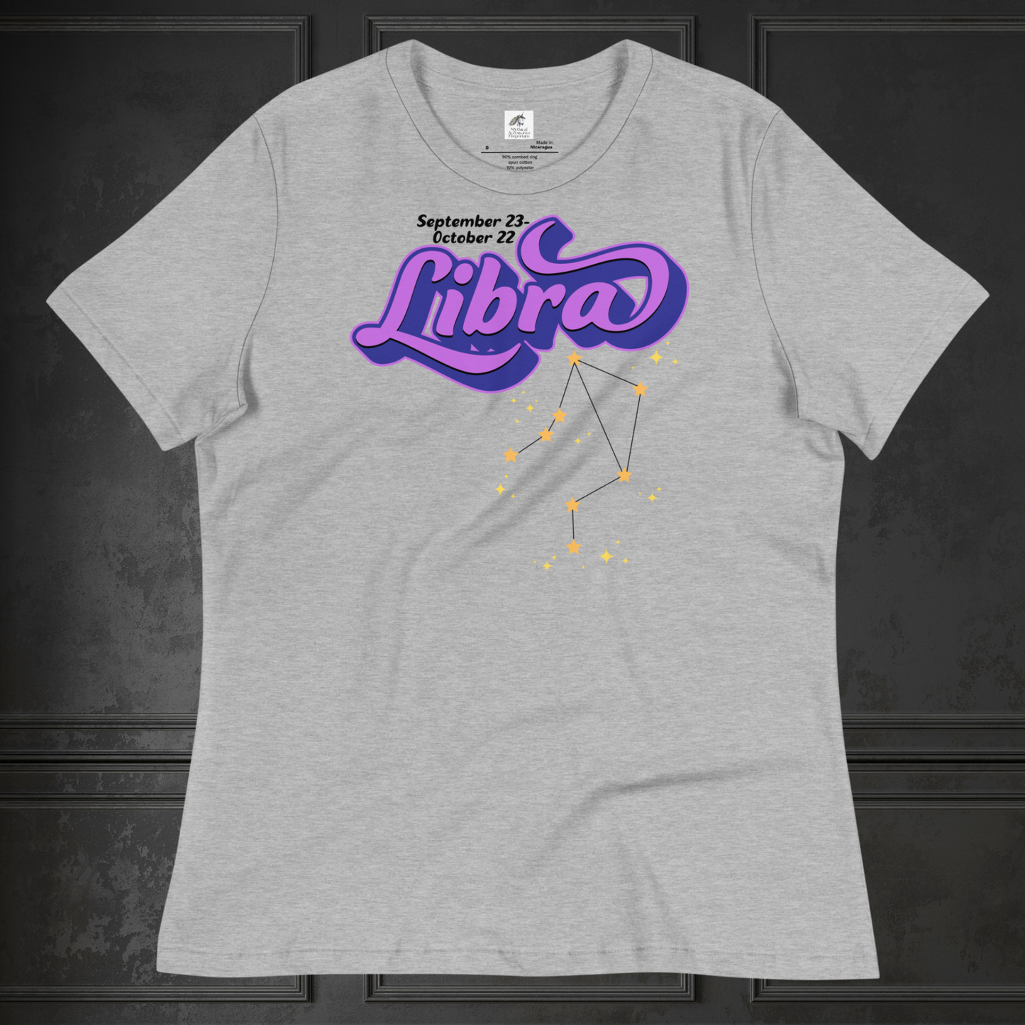 Front view of flat athletic heather (grey) women's Libra Tee. This astrology Libra T-Shirt has the word Libra in large purple script shadowed in deep blue for a 3-D effect. Below this it Says September 23-October 22. Under Libra is the zodiac star constellation with yellow stars connected by a black line and lighter yellow smaller stars surrounding this. The perfect October or September Birthday Gift for Her or yourself.