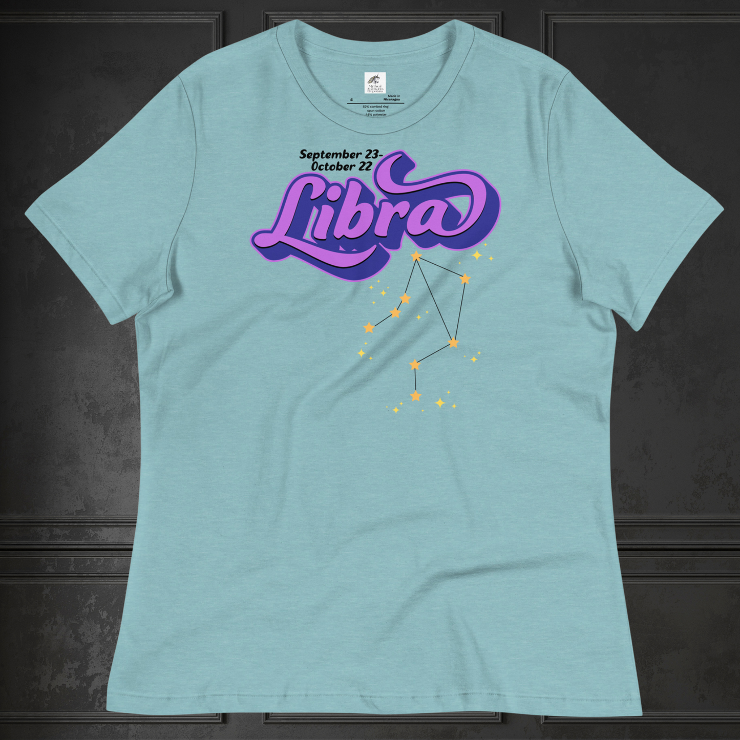 Front view of flat heather blue lagoon women's Libra Tee. This astrology Libra T-Shirt has the word Libra in large purple script shadowed in deep blue for a 3-D effect. Below this it Says September 23-October 22. Under Libra is the zodiac star constellation with yellow stars connected by a black line and lighter yellow smaller stars surrounding this. The perfect October or September Birthday Gift for Her or yourself.