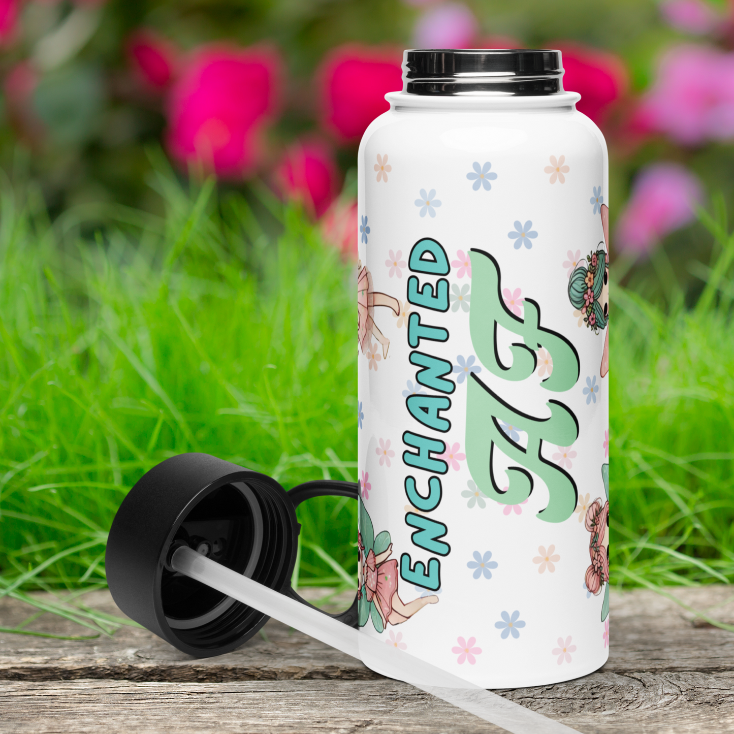 Front view of white fairy tumbler with black lid next to the bottle on the left side. YOu can see Enchanted AF. The silver colored steel is showing at the top where the lid screws on. You can see where the clear plastic straw is attached to the bottom of the lid.