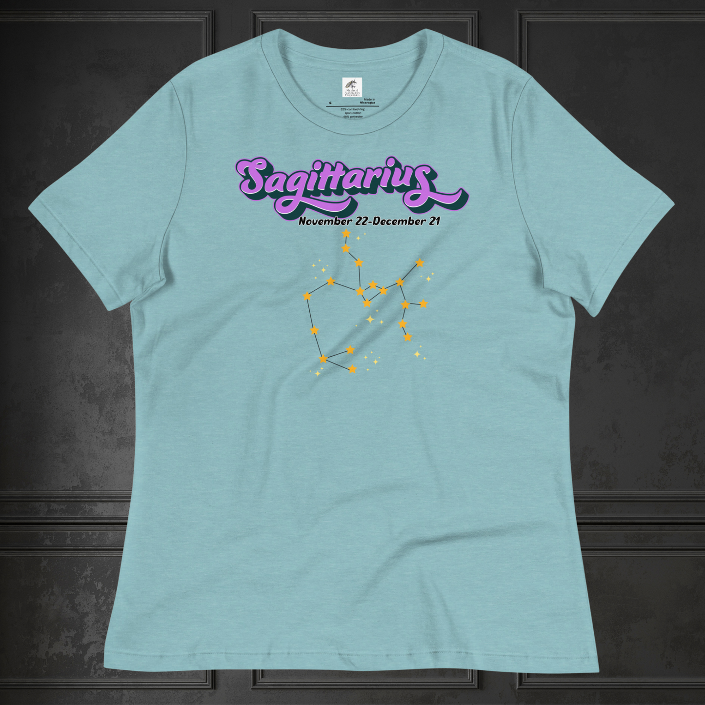 Front view of flat heather blue lagoon women's Sagittarius Tee. This astrology T-Shirt has the word Sagittarius in large purple script shadowed in black for a 3-D effect. Below this it Says November 22-December 21. Under Sagittarius is the zodiac star constellation with yellow stars connected by a black line and lighter yellow smaller stars surrounding this. The perfect November or December Birthday Gift for her or yourself.