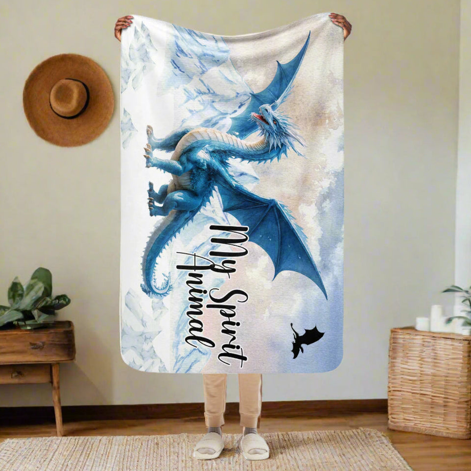 My Spirit Animal Dragon Blanket. Model holding blanket over her head size 37x57. Blanket bottom reaches her knees. This size is perfect for the car, traveling, or for children. Blue Ice Dragon with wings spread standing in front of snow capped mountain range with a dragon silhouette flying above. Ice Dragon Fantasy Bookish Gift, Dungeons and Dragons DND Dungeon Master Gift, Fantasy Home Decor