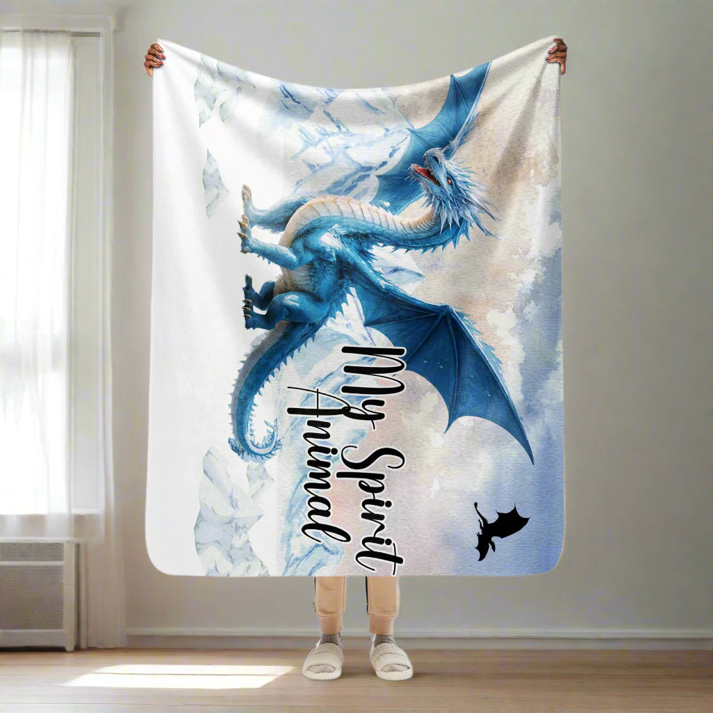 My Spirit Animal Dragon Blanket. Model holding blanket over her head size 50x60. Blanket is partially folded over at the top over her hands. Bottom of blanket reaches her knees. This is a couch throw size blanket perfect for cuddling up under on a chilly fall night. Blue Ice Dragon with wings spread standing in front of snow capped mountain range with a dragon silhouette flying above. Ice Dragon Fantasy Bookish Gift, Dungeons and Dragons DND Dungeon Master Gift, Fantasy Home Decor