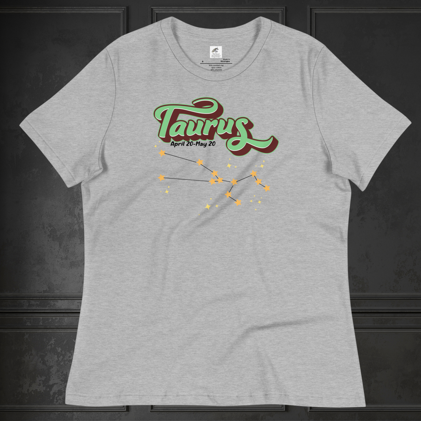 Front view of athletic heather (grey) Taurus Tee laying flat on a black surface. You can see the crew neck collar and short sleeves of the t shirt. This Astrology T-Shirt has the word Taurus in large leaf green script shadowed in deep brown for a 3-D effect. Below this it Says April 20-May 20. At the bottom is the star constellation for Taurus with yellow stars connected by a black line and smaller stars surrounding the constellation. The perfect April or May Birthday Gift for Her or yourself.