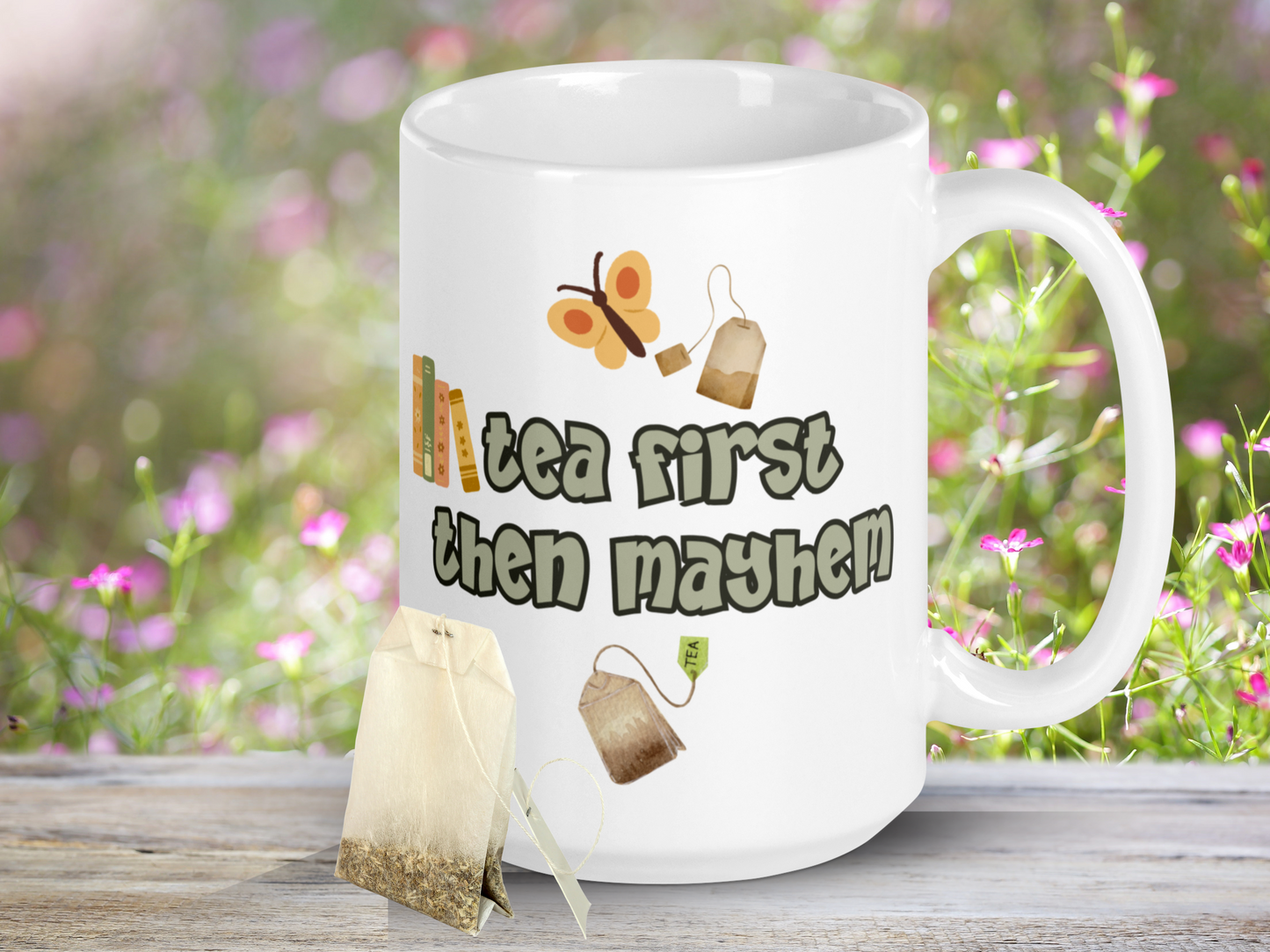 Ceramic Dragon Mug with handle to the right. In light green outlined in black are the words, "tea first then mayhem". Sitting on the word then like a bookshelf are 4 books. Above the words is a yellow butterfly and a tea bag. Below the words is a tea bag.