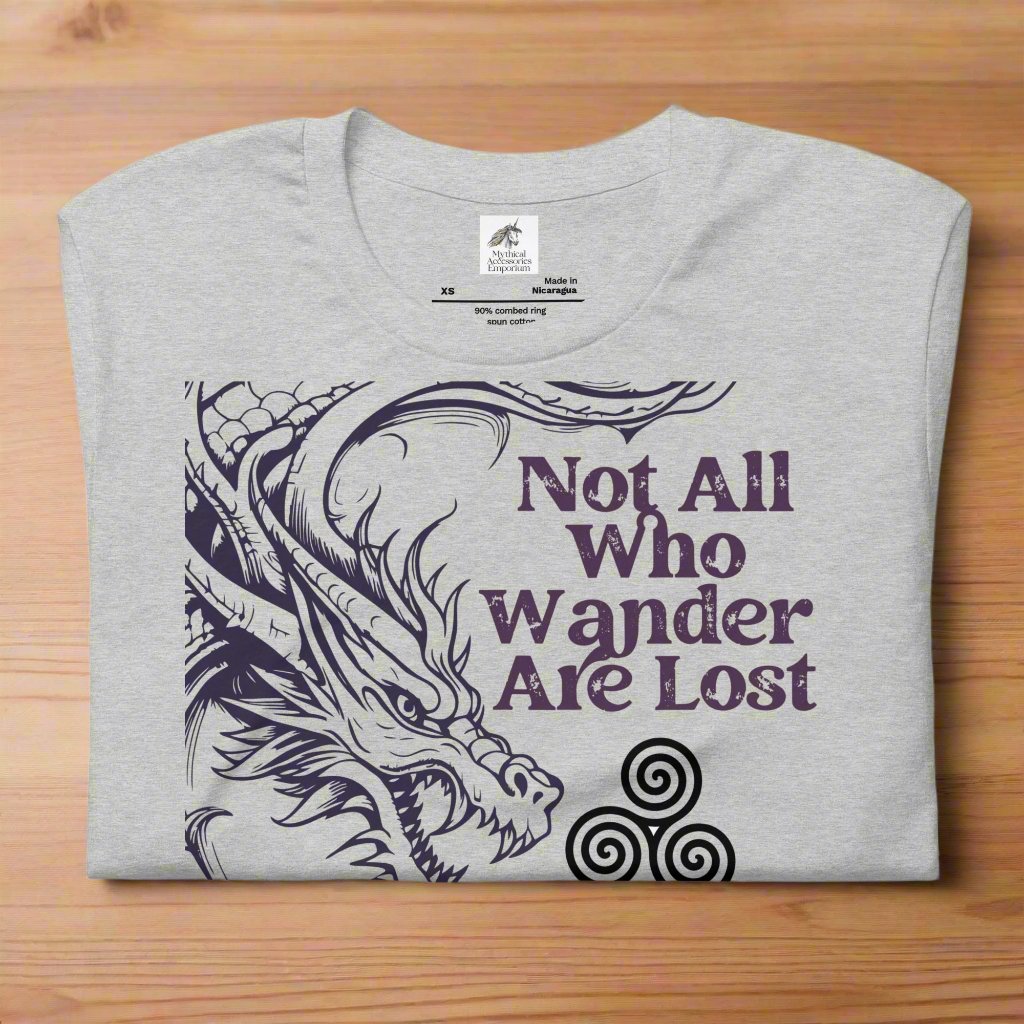 athletic heather (grey) men’s T-shirt, front view folded on counter. Right side features a dragon in smoky gray-purple with the Celtic triskele symbol emerging from its nostrils. Text above reads "Not All Who Wander Are Lost," with "Some Are Looking for Dragons" below.