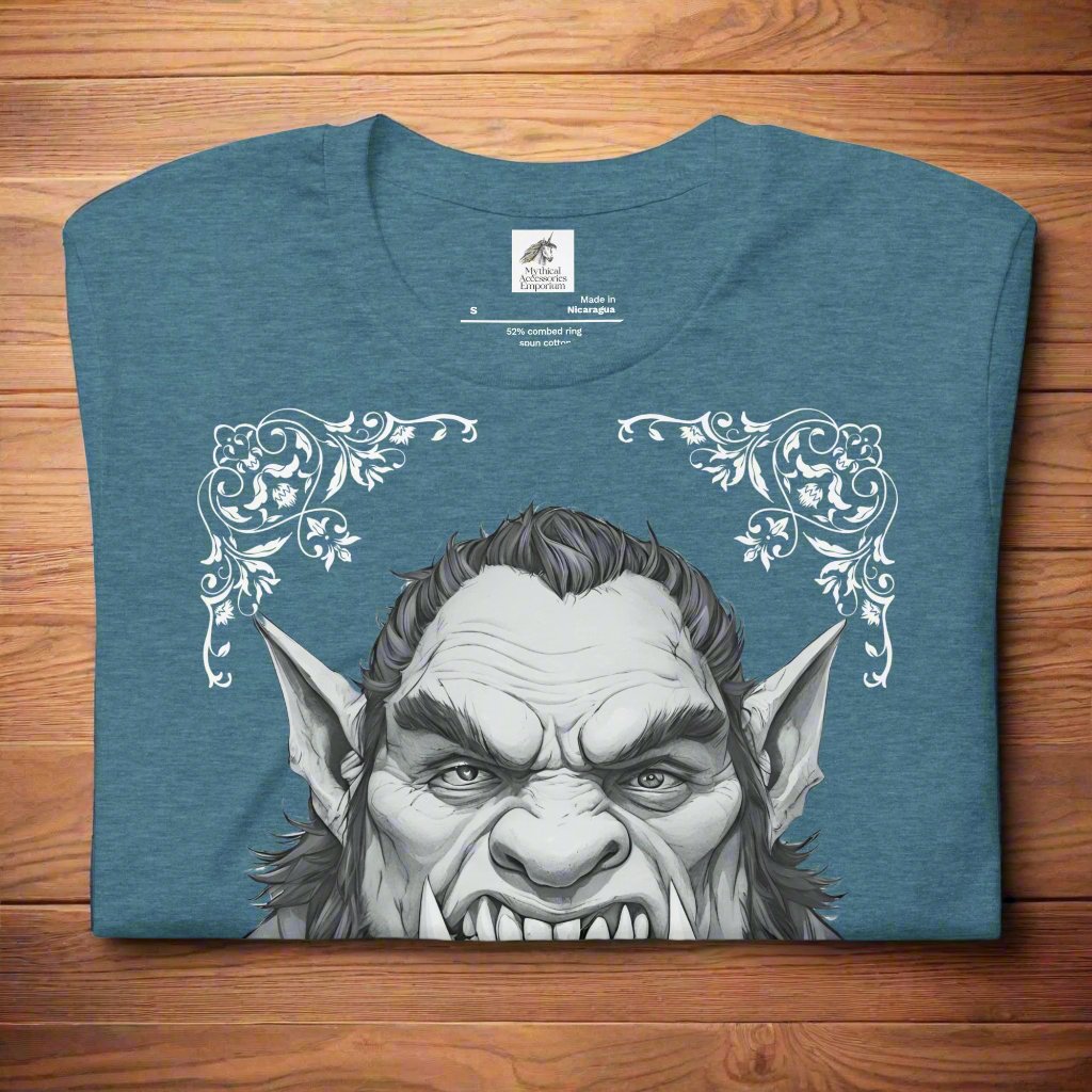 Front view of flat folded Men's heather deep teal Graphic Tee with a black and white orc on the front. The orcs lower canines jut up as tusks over his top lip. He has a bulbous nose, eyebrows drawn down into a fierce expression, a large forehead, large pointed ears, his hair is black and pulled back with a widows peak, he has hair down the sides of his face and a medium sized beard. Framing the orc in four corners is 1920s retro floral border in dark green. This is a regular fit men's tshirt