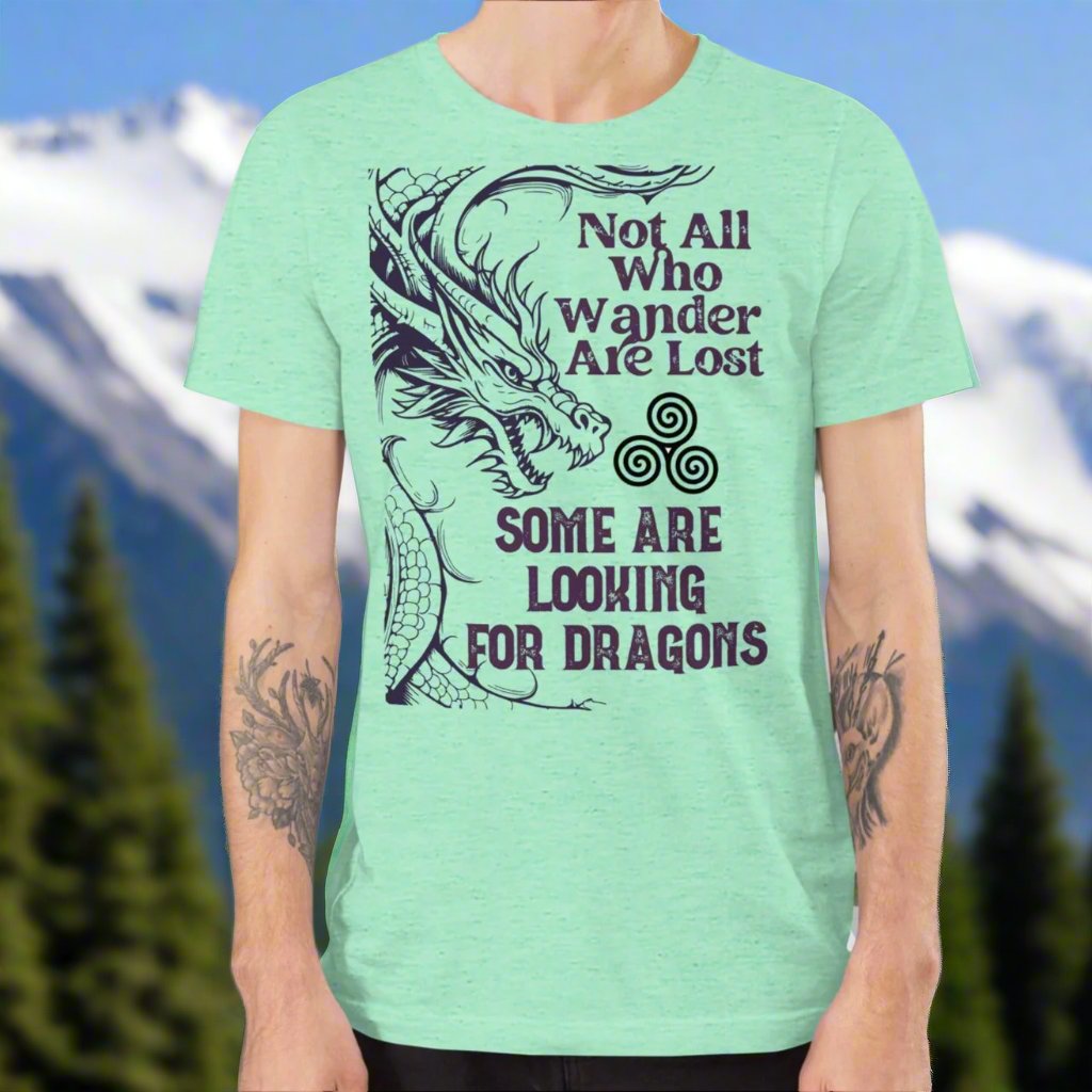 Heather mint men’s T-shirt, front view. Right side features a dragon in smoky gray-purple with the Celtic triskele symbol emerging from its nostrils. Text above reads "Not All Who Wander Are Lost," with "Some Are Looking for Dragons" below.