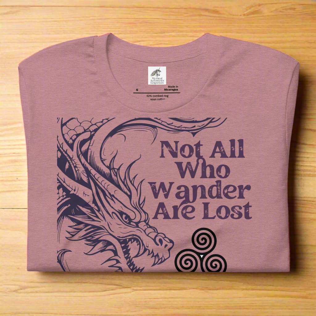Heather orchid men’s T-shirt, front view folded on a counter. Right side features a dragon in smoky gray-purple with the Celtic triskele symbol emerging from its nostrils. Text above reads "Not All Who Wander Are Lost," with "Some Are Looking for Dragons" below.