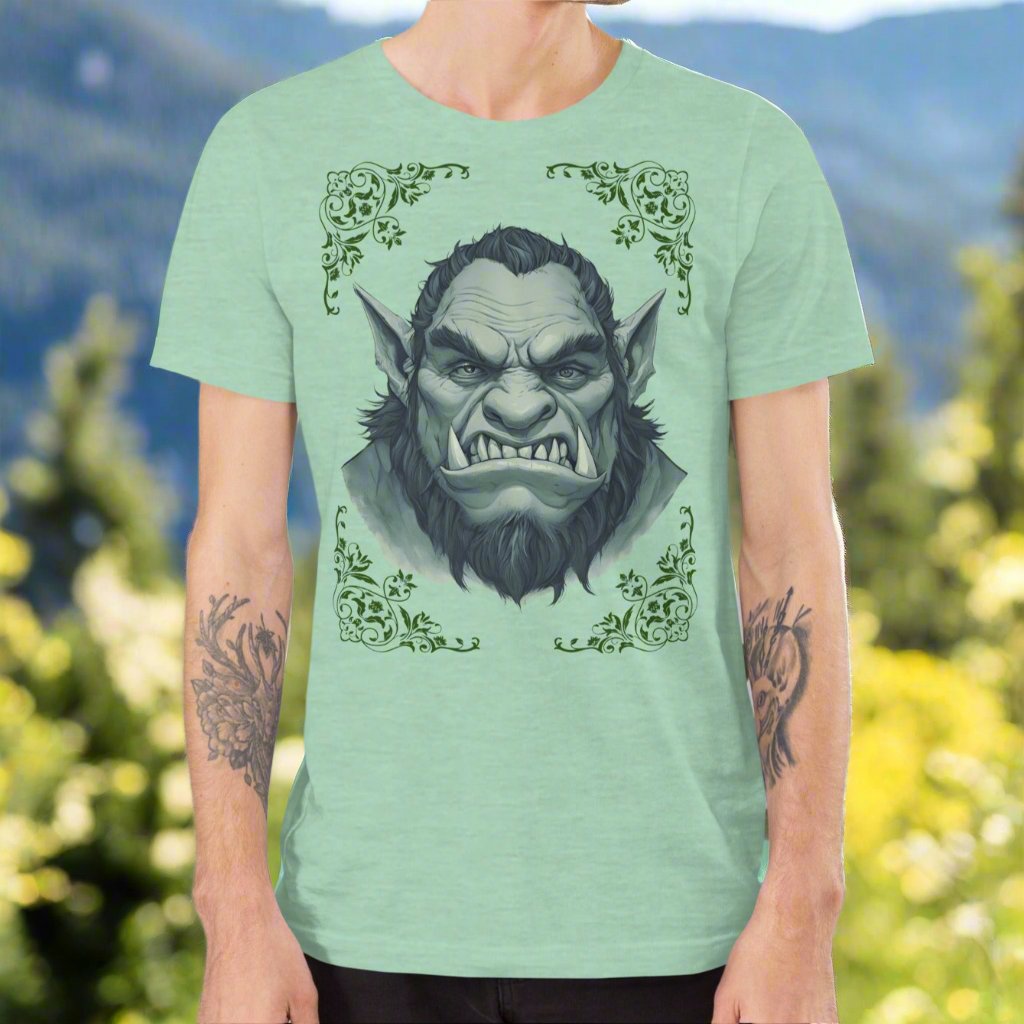 Front view of Men's Heather Prism Mint Graphic Tee with a black and white orc on the front. The orcs lower canines jut up as tusks over his top lip. He has a bulbous nose, eyebrows drawn down into a fierce expression, a large forehead, large pointed ears, his hair is black and pulled back with a widows peak, he has hair down the sides of his face and a medium sized beard. Framing the orc in four corners is 1920s retro floral border in dark green. This is a regular fit men's tshirt or a unisex shirt.