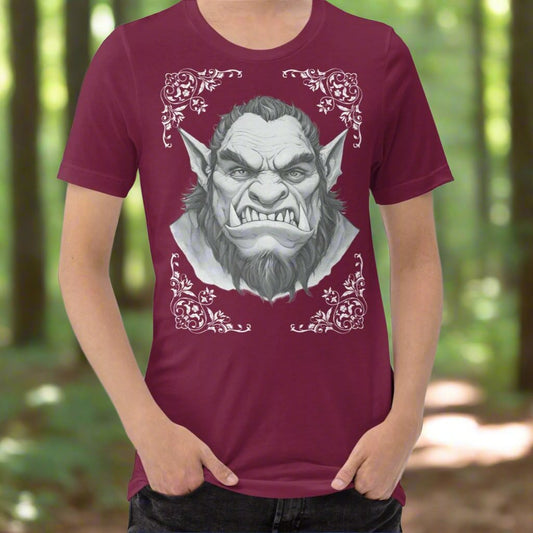 Front view of Men's maroon Graphic Tee with a black and white orc on the front. The orcs lower canines jut up as tusks over his top lip. He has a bulbous nose, eyebrows drawn down into a fierce expression, a large forehead, large pointed ears, his hair is black and pulled back with a widows peak, he has hair down the sides of his face and a medium sized beard. Framing the orc in four corners is 1920s retro floral border in dark green. This is a regular fit men's tshirt or a unisex shirt.