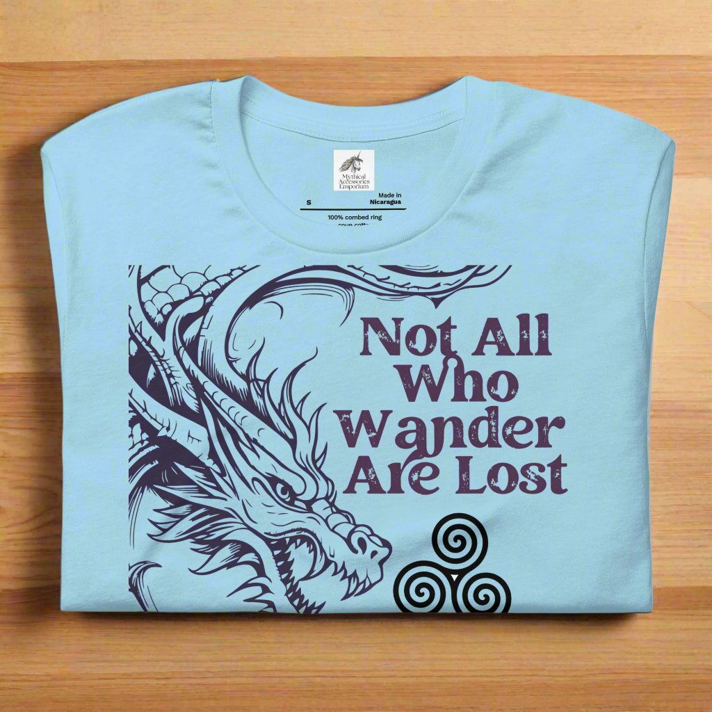 ocean blue men’s T-shirt folded on counter, front view. Right side features a dragon in smoky gray-purple with the Celtic triskele symbol emerging from its nostrils. Text above reads "Not All Who Wander Are Lost," with "Some Are Looking for Dragons" below.