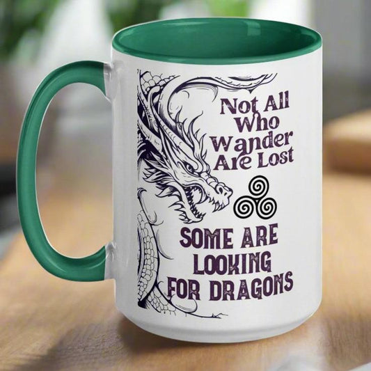 Ceramic Mug, handle to left, dark green interior and handle. Dark Purple Grey dragon on left with a triskelion (three spiral circle) coming out of the mouth. The Triskelion symbol represents the circle of birth, life, and death. Above the symbol Not All Who Wander Are Lost. Below the symbol Some Are Looking for Dragons.