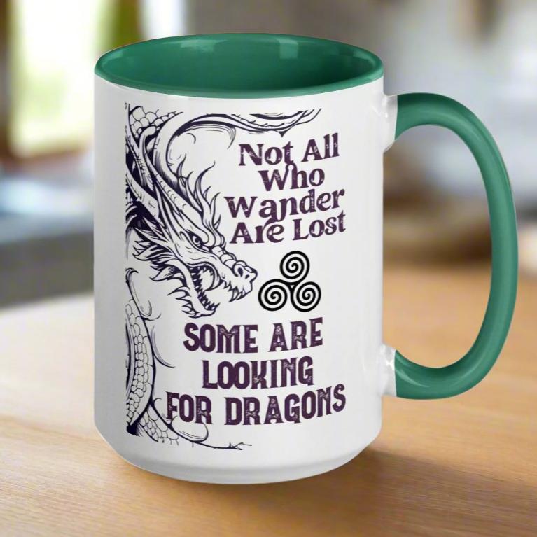 Ceramic Mug, handle to right, dark green interior and handle. Dark Purple Grey dragon on left with a triskelion (three spiral circle) coming out of the mouth. The Triskelion symbol represents the circle of birth, life, and death. Above the symbol Not All Who Wander Are Lost. Below the symbol Some Are Looking for Dragons.
