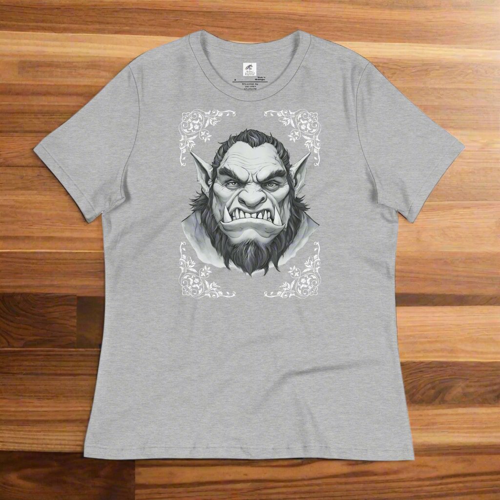 Orc Women's T-Shirt, athletic heather (grey), lay front front view on wood counter. Flower corner borders in white frame a black and white image a fierce Orc. Bearded, tusk like teeth, and pointed ears of a deadly fae.