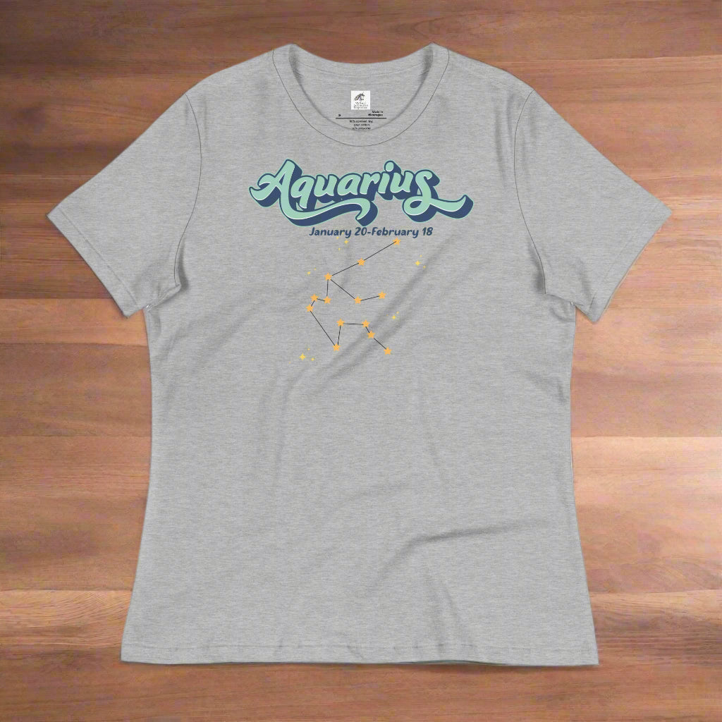 Flat lay athletic heather grey astrology Aquarius T-shirt on a wooden counter. At the top in light blue is the word Aquarius outlined in deeper blue. Below this it says January 20- February 18. Under this is the Aquarius constellation with orange yellow stars connected by a black line. Astrology Zodiac Aquarius Woman's Tee