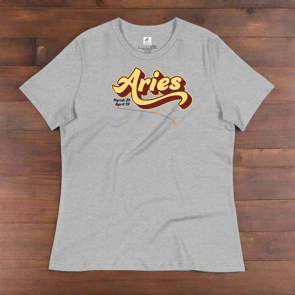Aries Tee laying flat on a wooden counter, athletic heather (grey). On the top is the word Aries in light yellow lined with maroon. Under the A are the dates March 21-April 19. Below his is the constellation Aries in bright yellow orange stars connected with a black line. Aries constellation zodiac astrology sign.